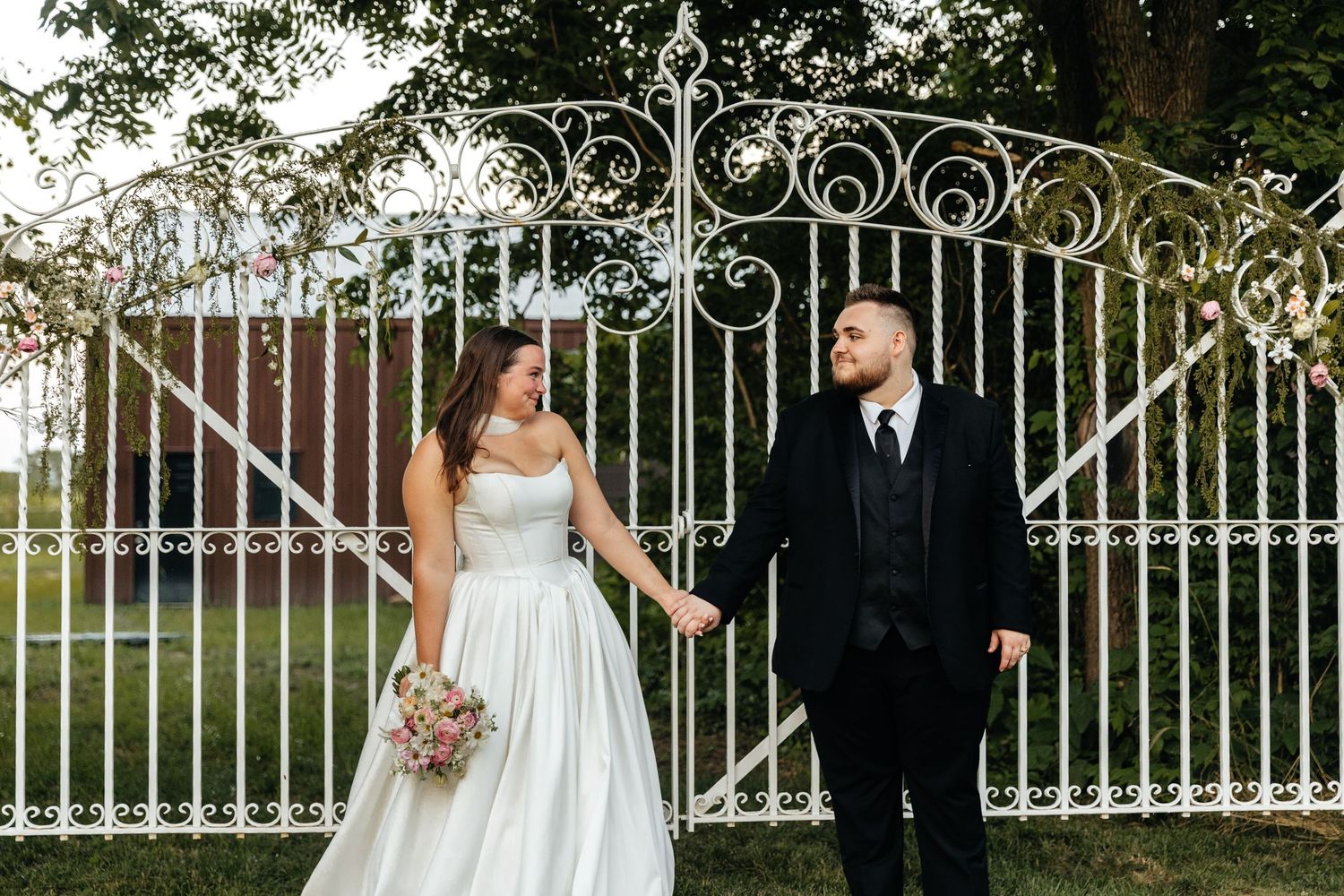 Elegant wedding photo session by ornate white iron gates and brick columns at sunset.