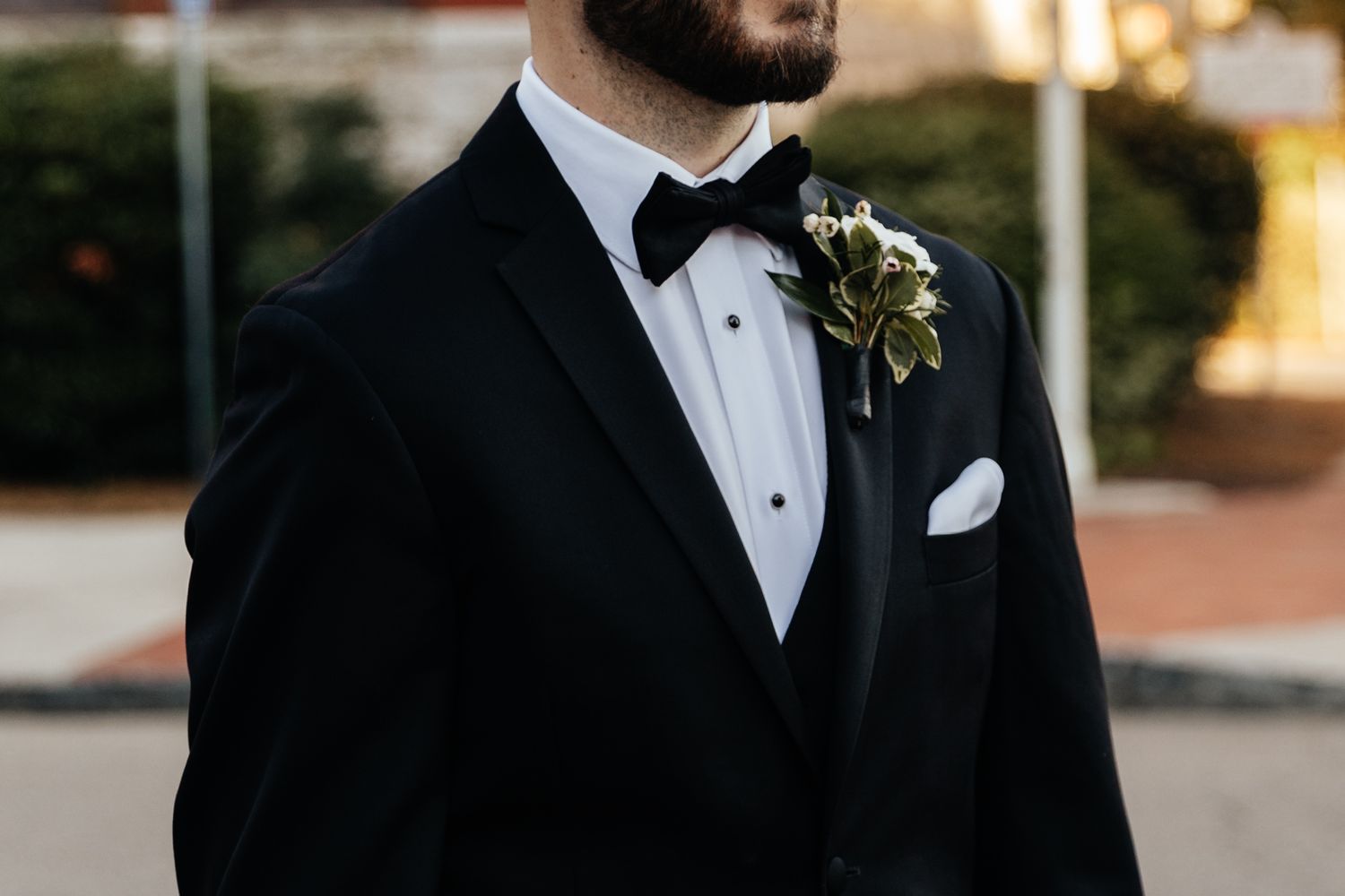 Close-up details of formal black tuxedo with white boutonniere against dark background.