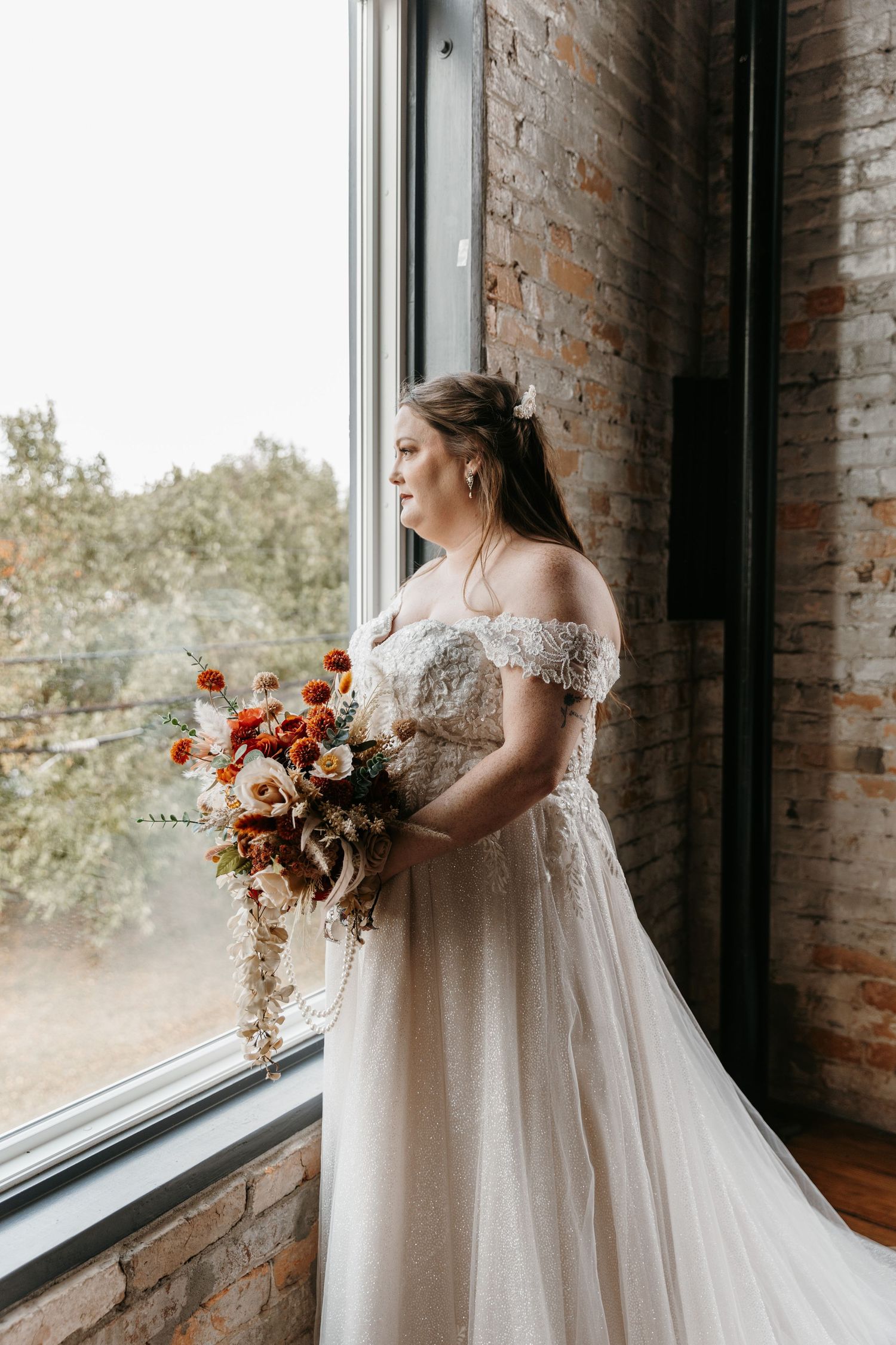 An elegant bridal photo against exposed brick walls and large windows with fall-colored bouquet.