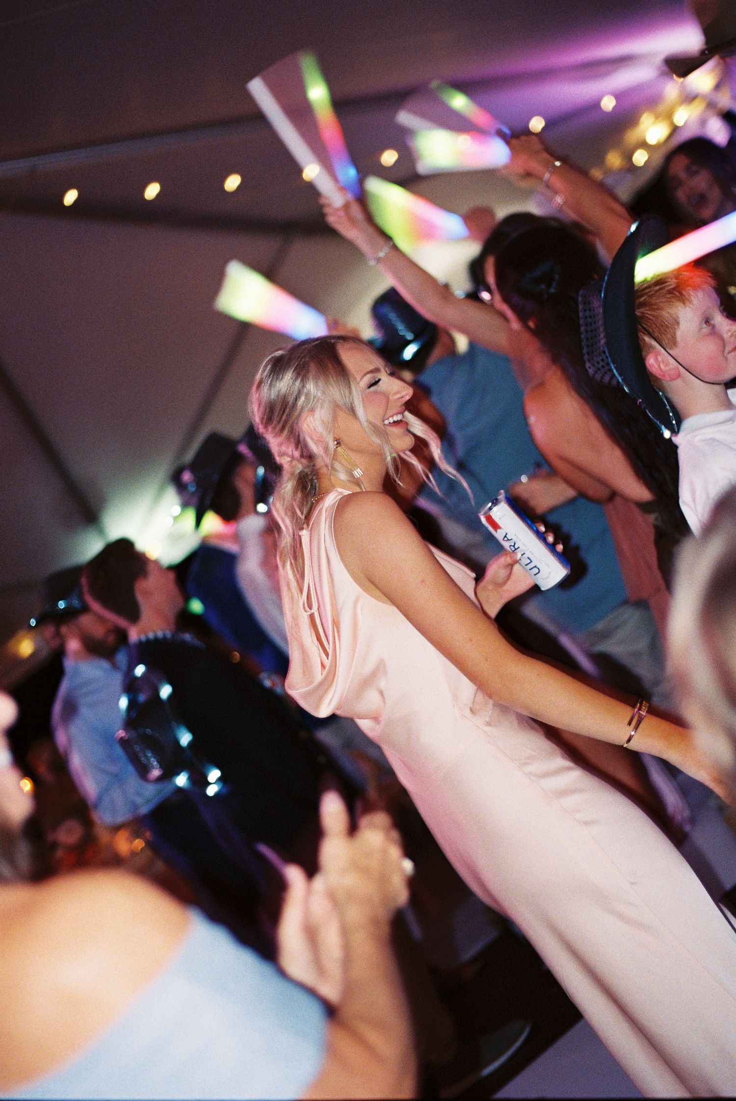 Guests dancing with glowing foam sticks at a lively wedding reception under a tent.