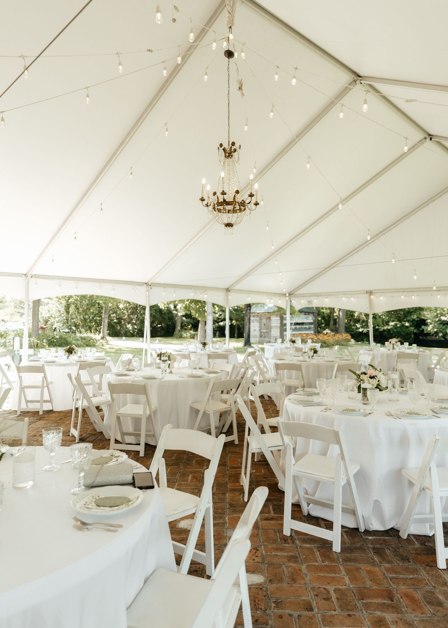 White wedding reception tent setup with elegant table settings and string lights overhead.
