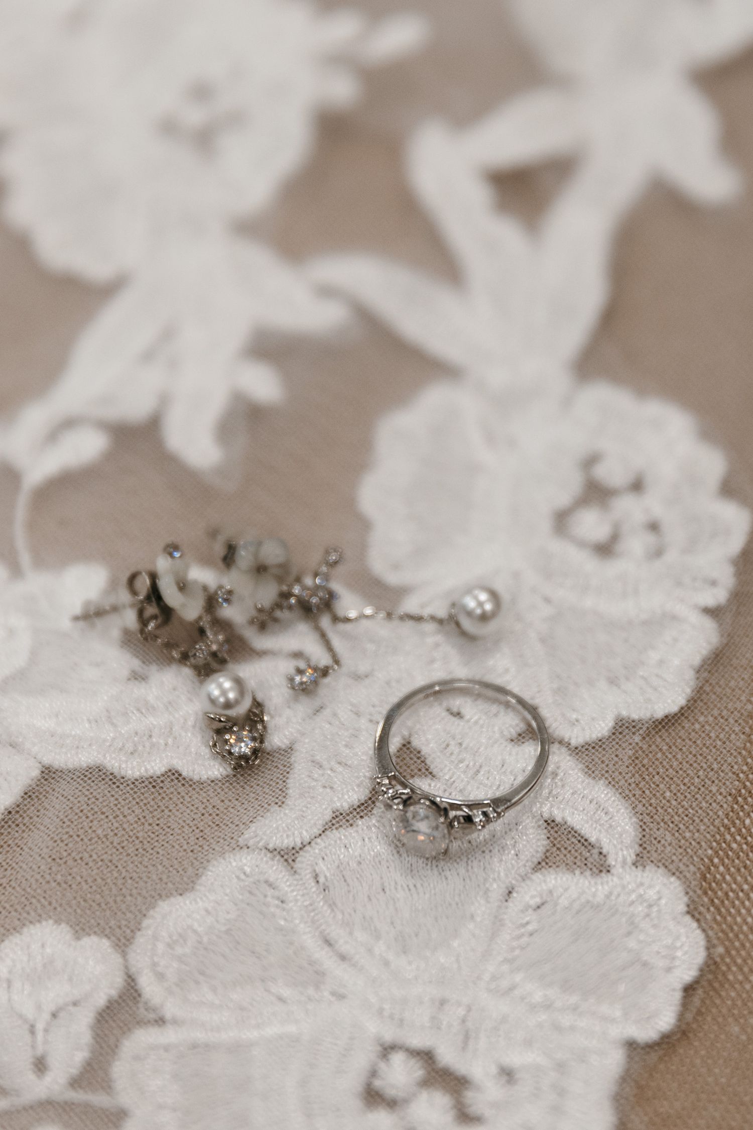 Wedding rings and jewelry arranged on delicate white lace against a neutral background.