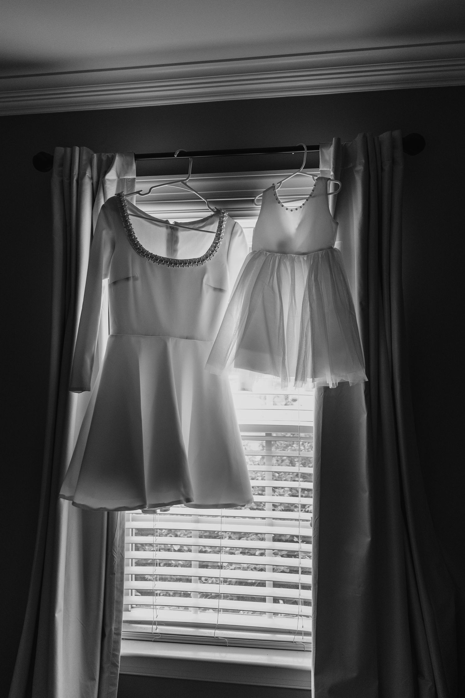 Black and white photo of white dresses hanging by window with natural light.