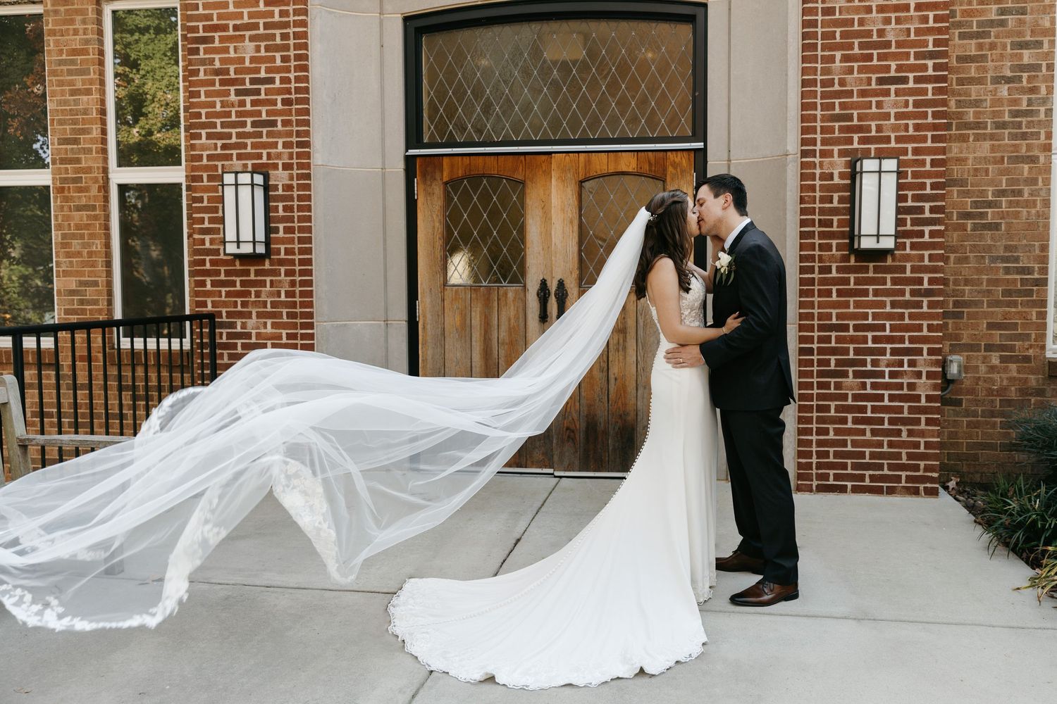 Wedding couple with flowing veil captured in front of ornate wooden doors.