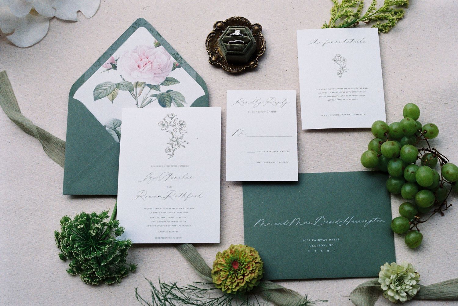 Elegant wedding stationery flat lay with green envelopes and botanical details.