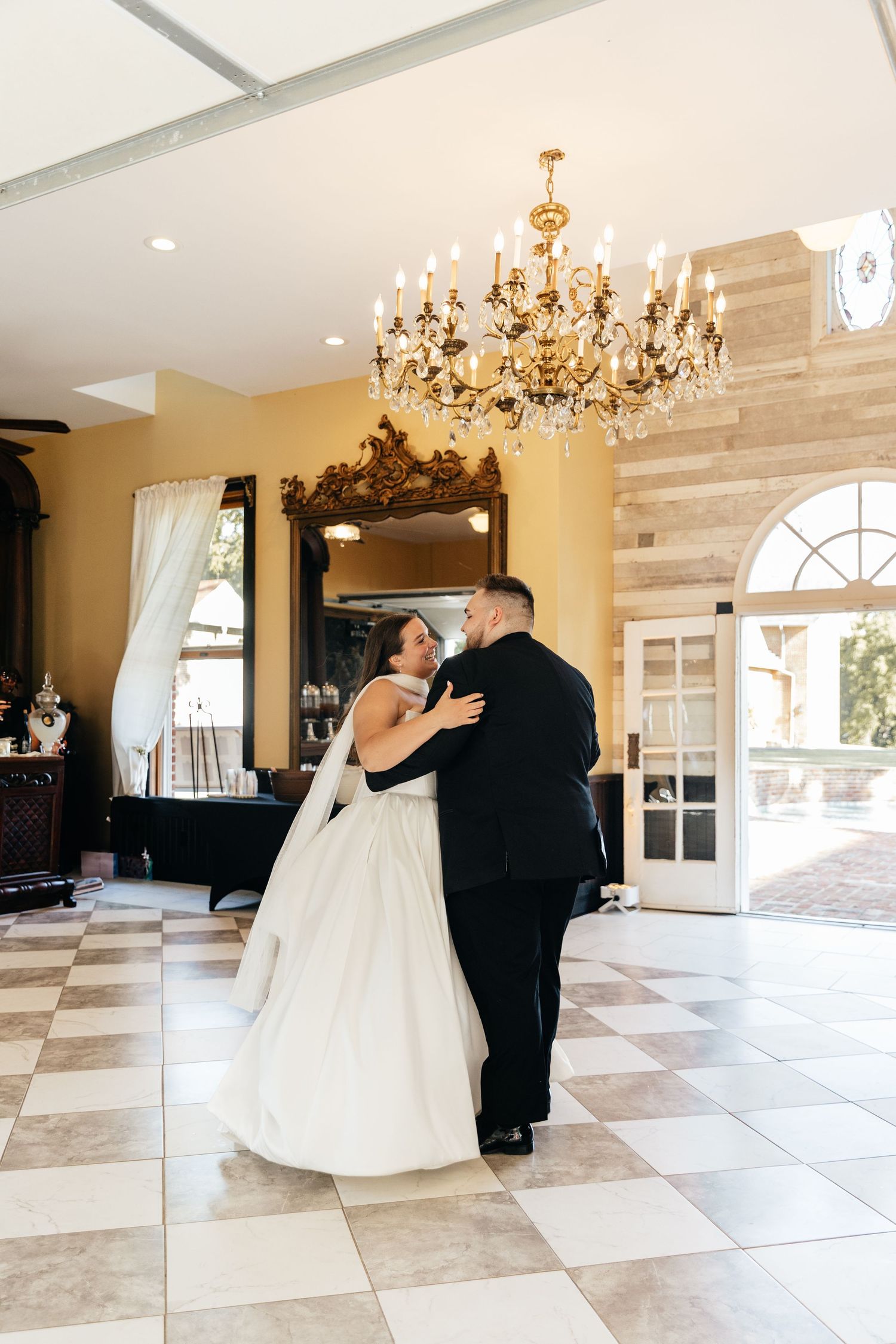 Elegant ballroom with chandelier and checkered marble floor during wedding celebration.