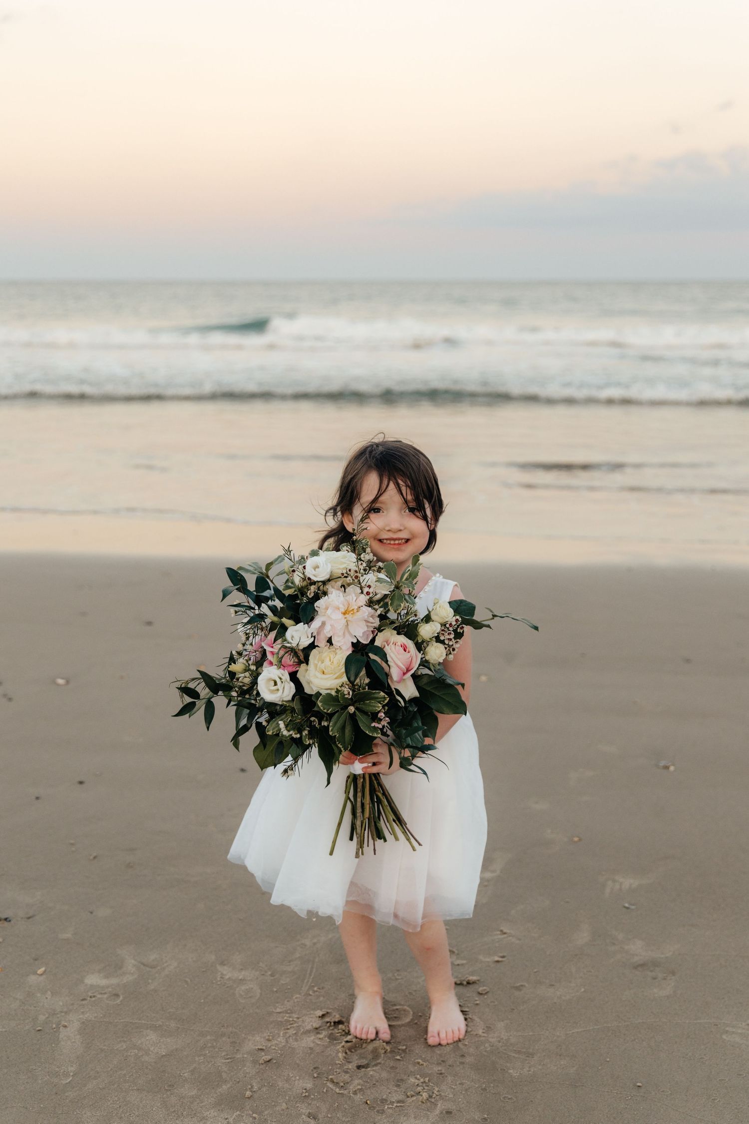 A girl holds the bride's bouquet while standing on the beach.