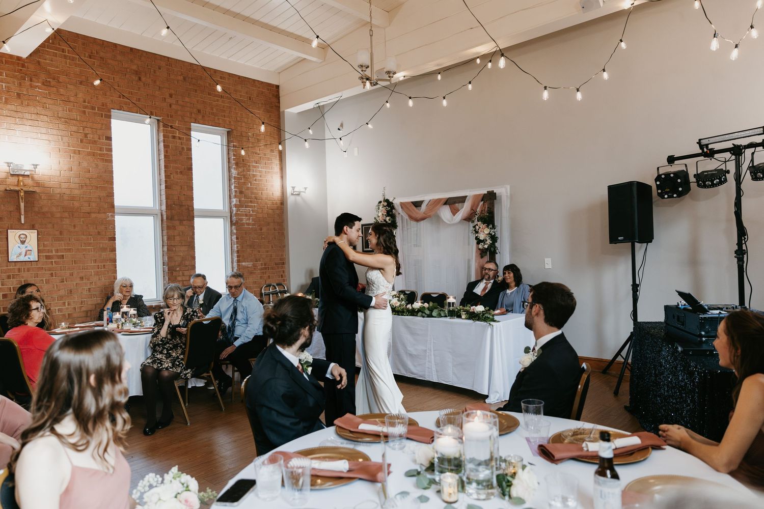 Reception venue decorated with string lights and white tablecloths during wedding celebration.