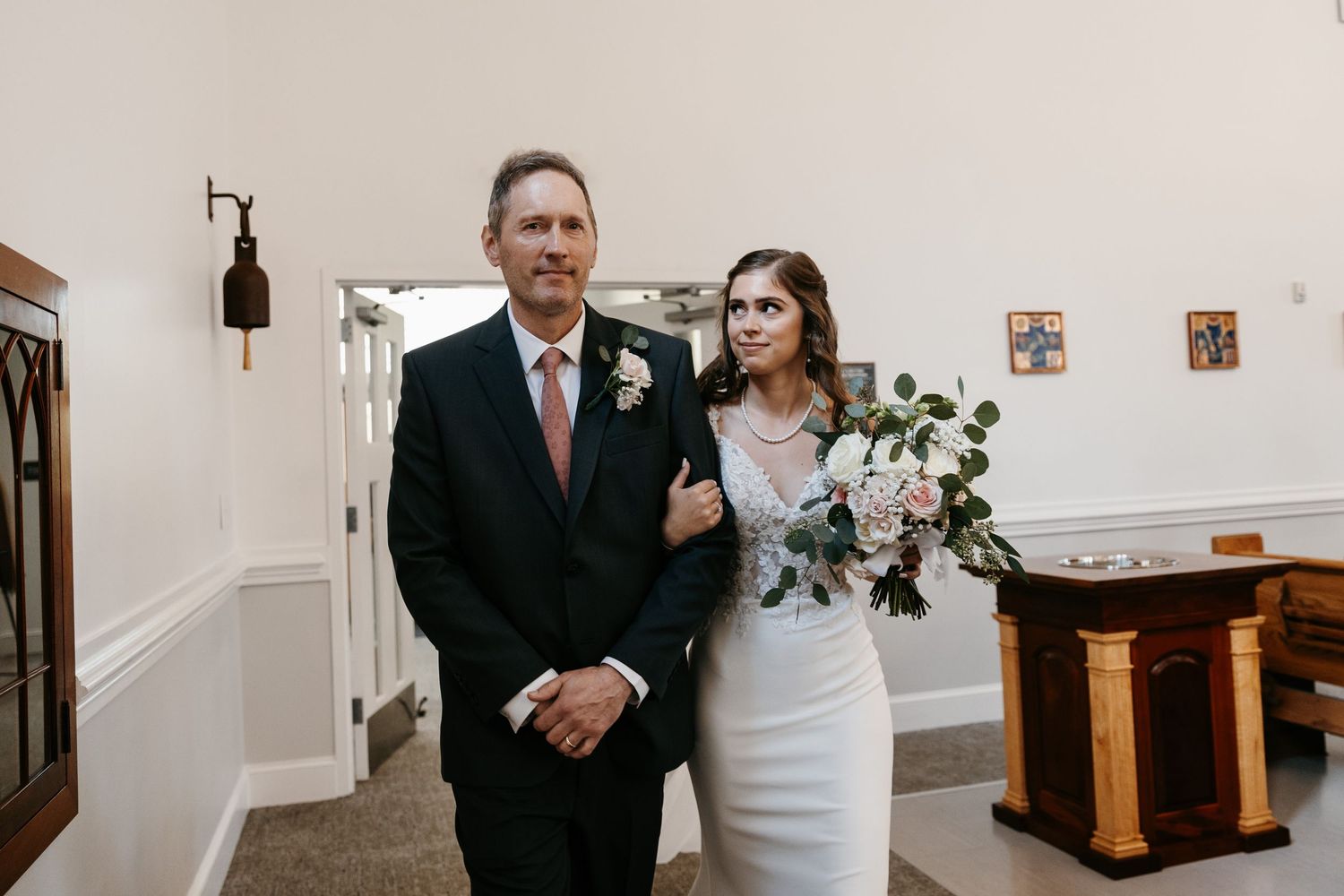 A wedding processional walking through a church hallway with elegant decor.