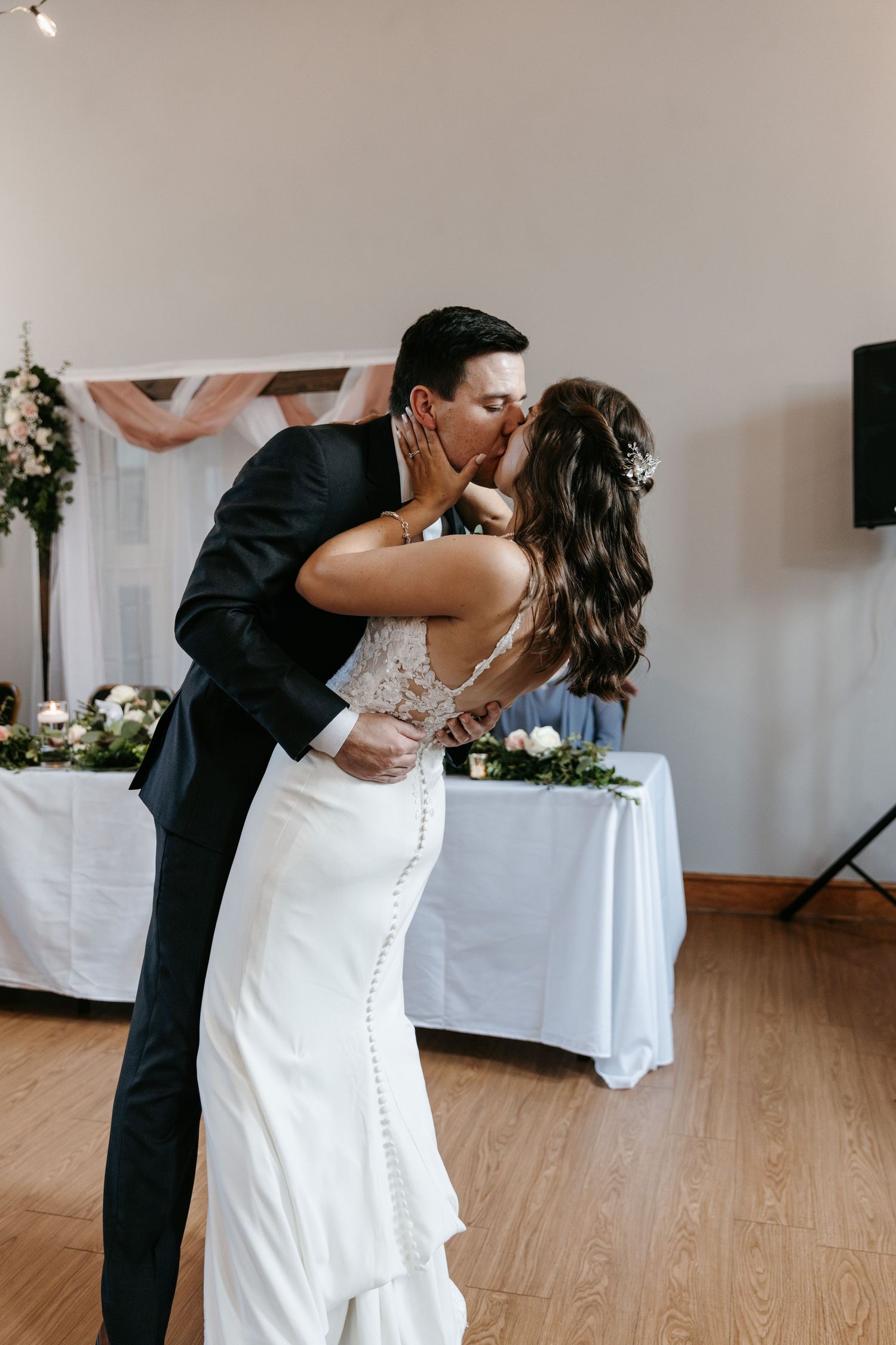Romantic dip during first dance at wedding reception with string lights and white decor.