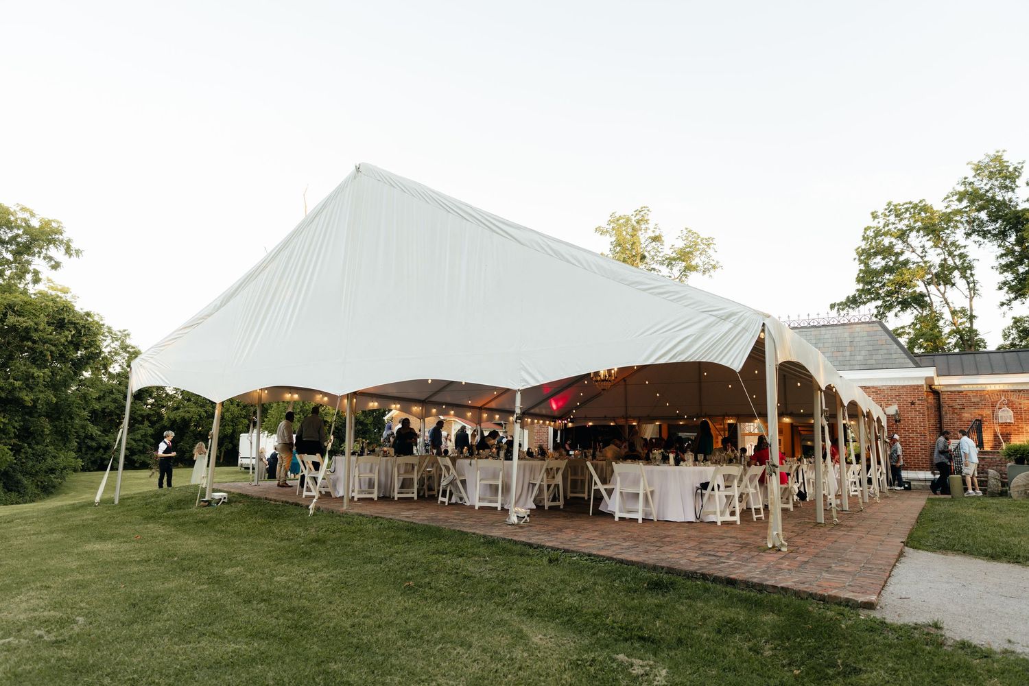 Large white wedding reception tent set up on a sprawling green lawn.