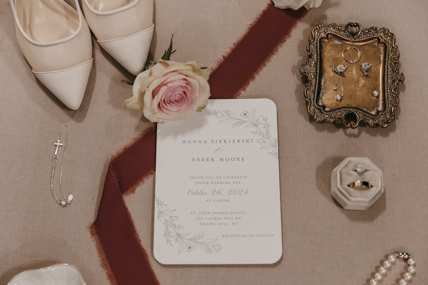Wedding details flatlay with invitations, jewelry, shoes, and roses on beige background.
