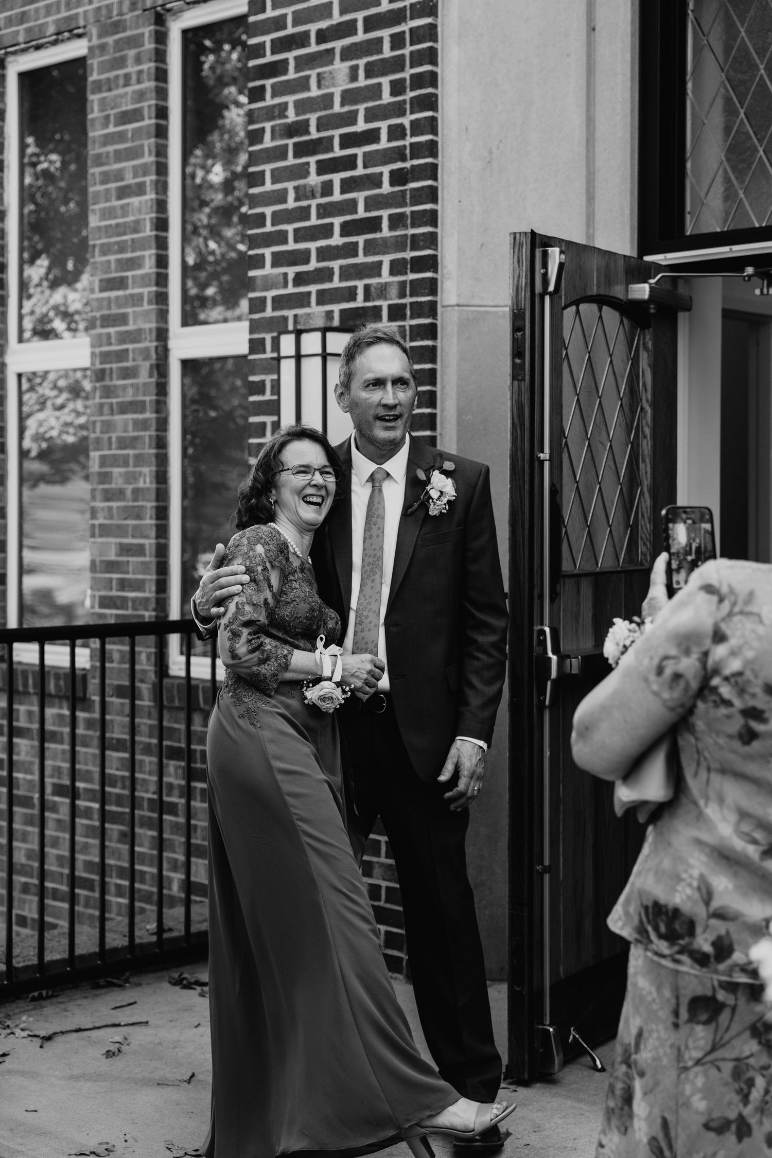 Black and white photo of couple laughing outside brick building entrance.