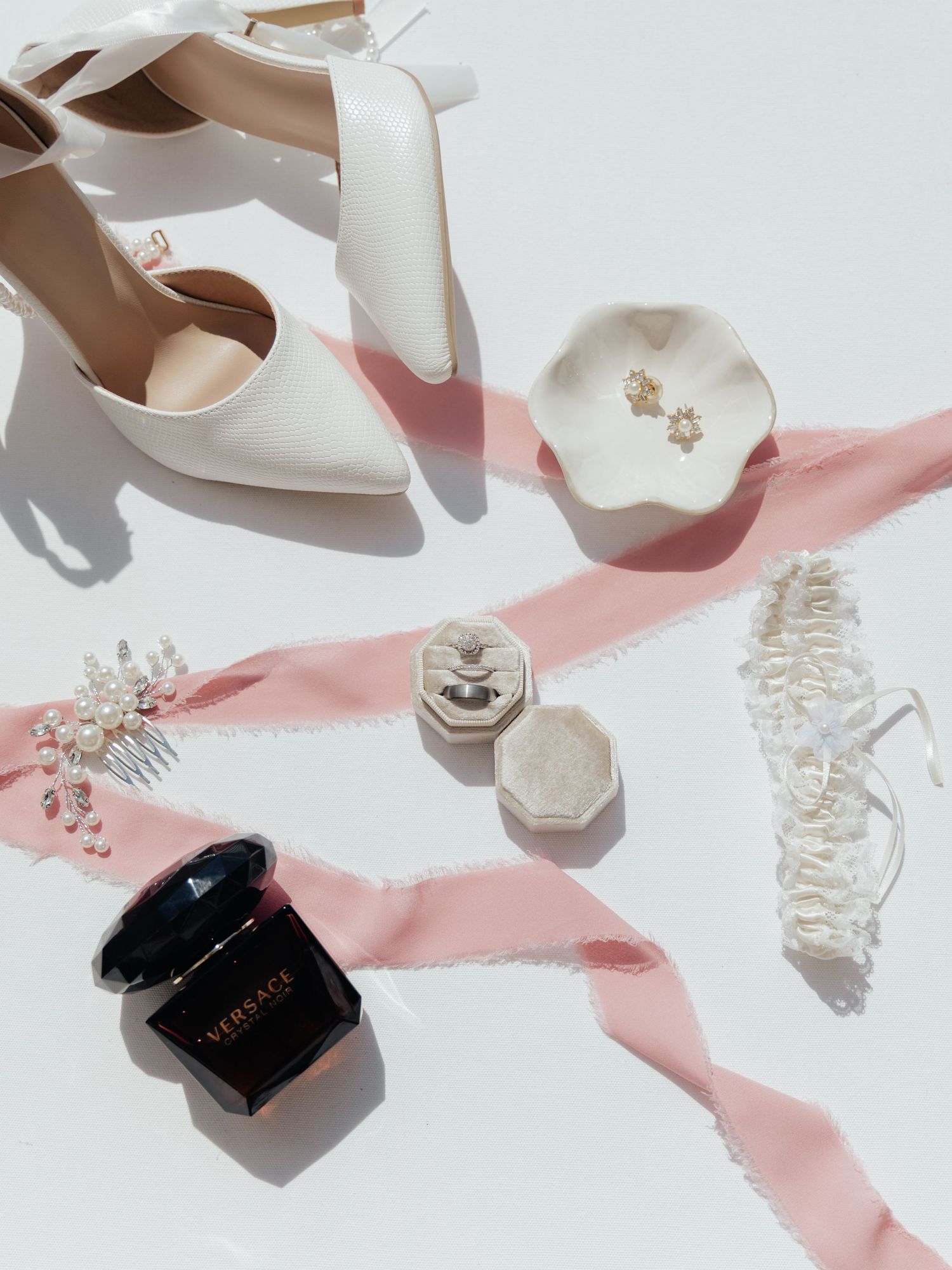 Wedding accessories including white heels, jewelry and pink ribbon on white background.