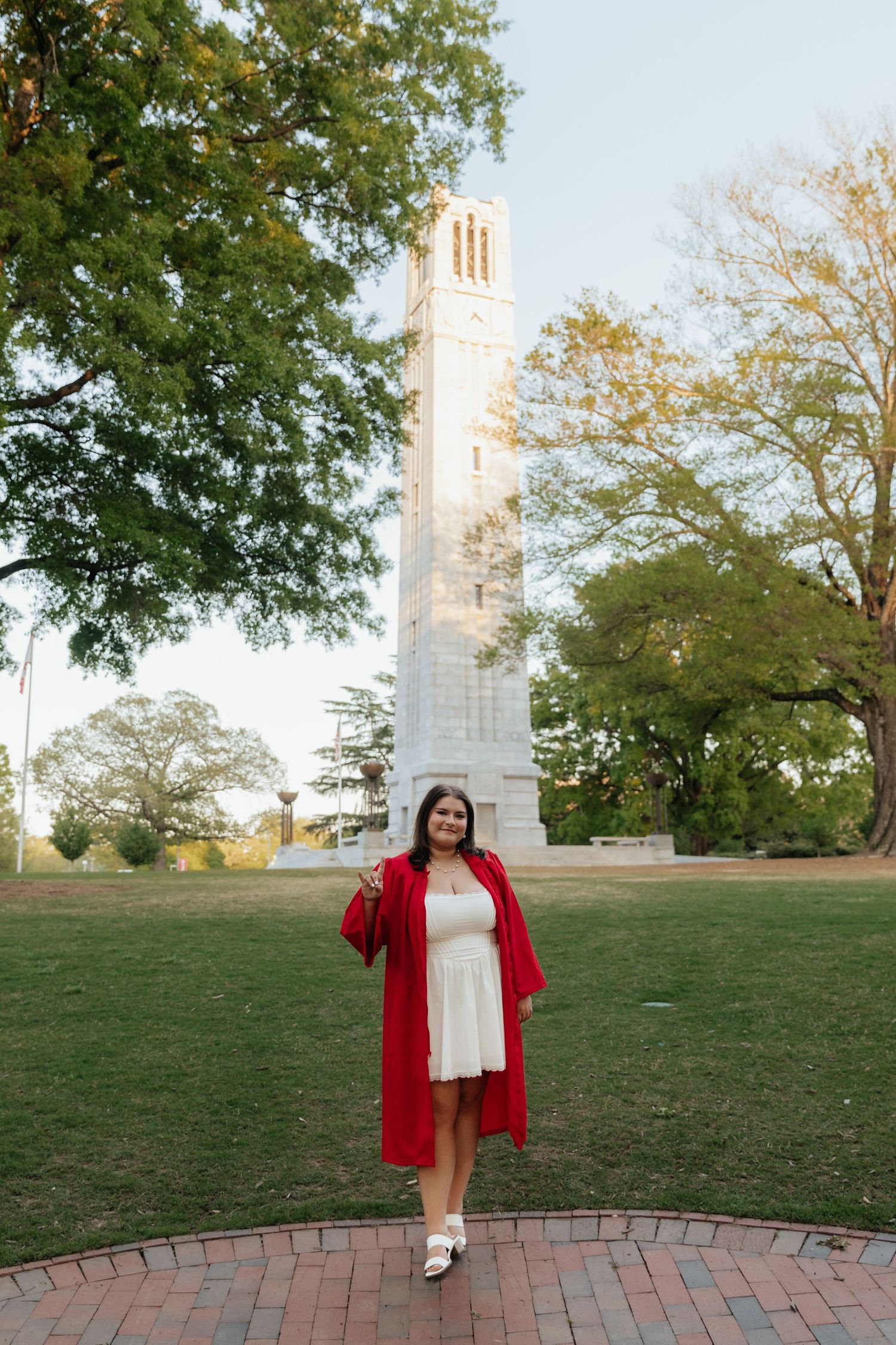 Graduate in red and white attire posing in front of bell tower.