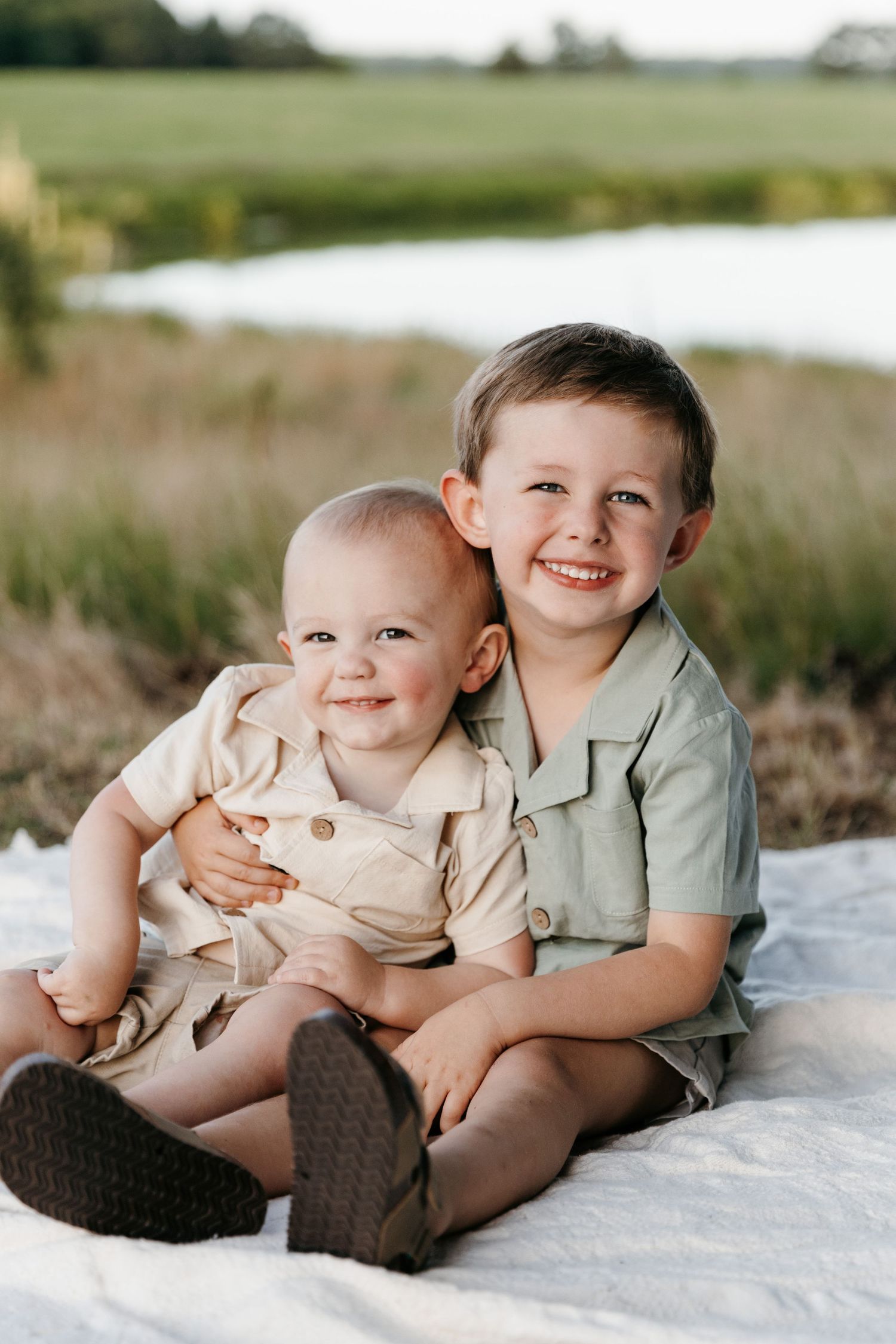 Two young siblings in coordinating outfits sitting together on a blanket outdoors.
