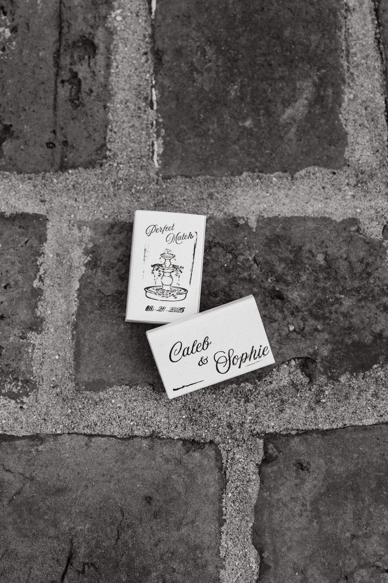 Custom matchbooks arranged on textured brick surface captured in black and white.