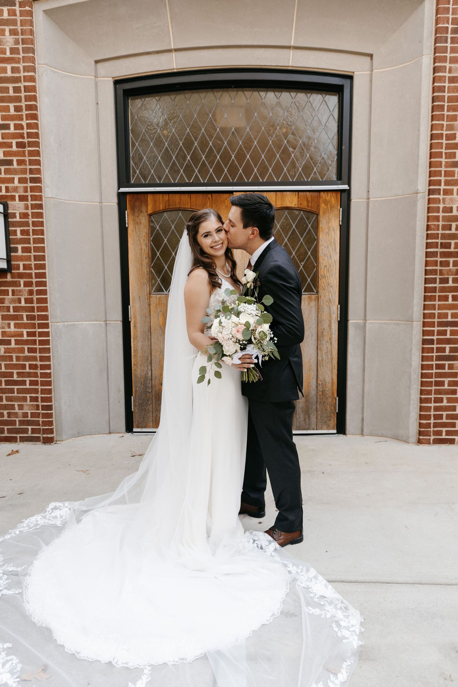 Wedding portraits showcasing a flowing lace veil against classic brick architecture.