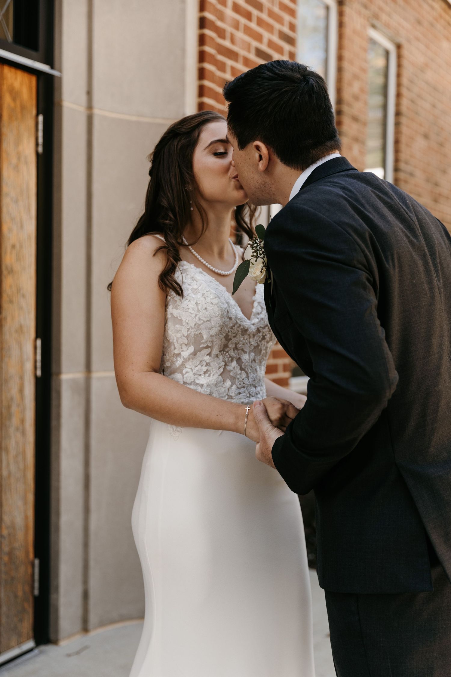 Romantic wedding couple sharing intimate moment against brick wall backdrop.