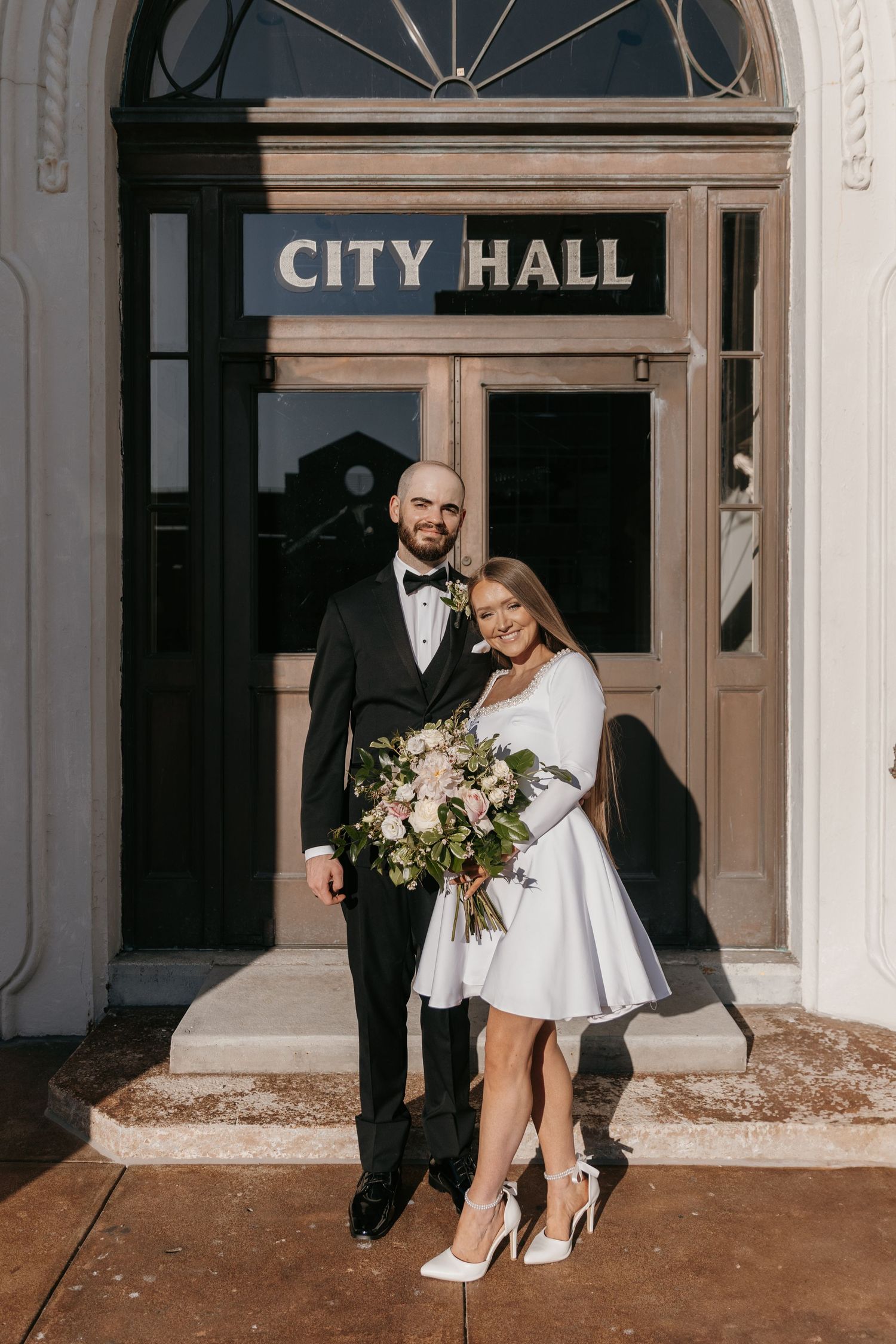 A couple poses for their wedding portrait in front of a classic City Hall entrance.