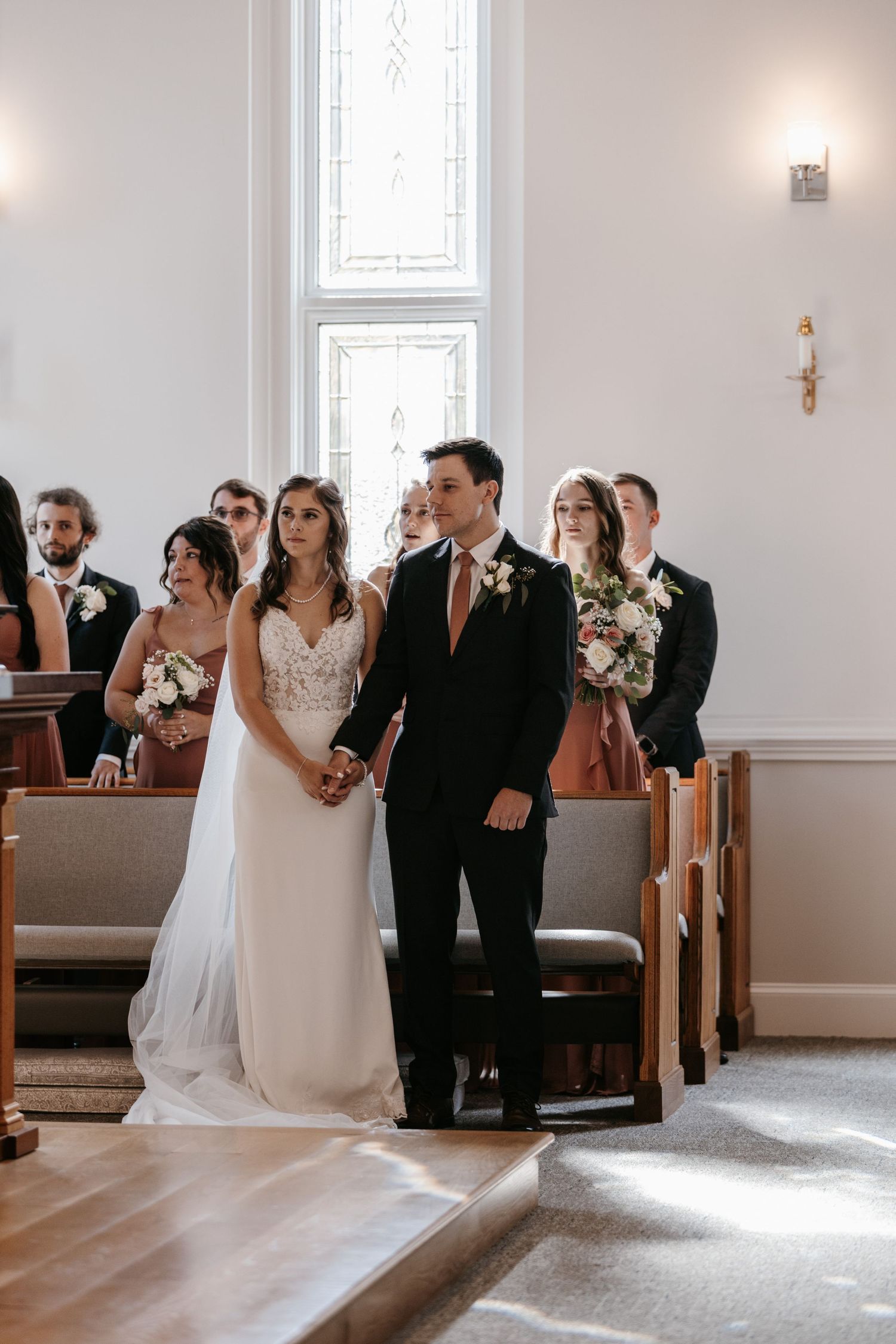 A wedding ceremony in a bright church sanctuary with tall windows and white walls.
