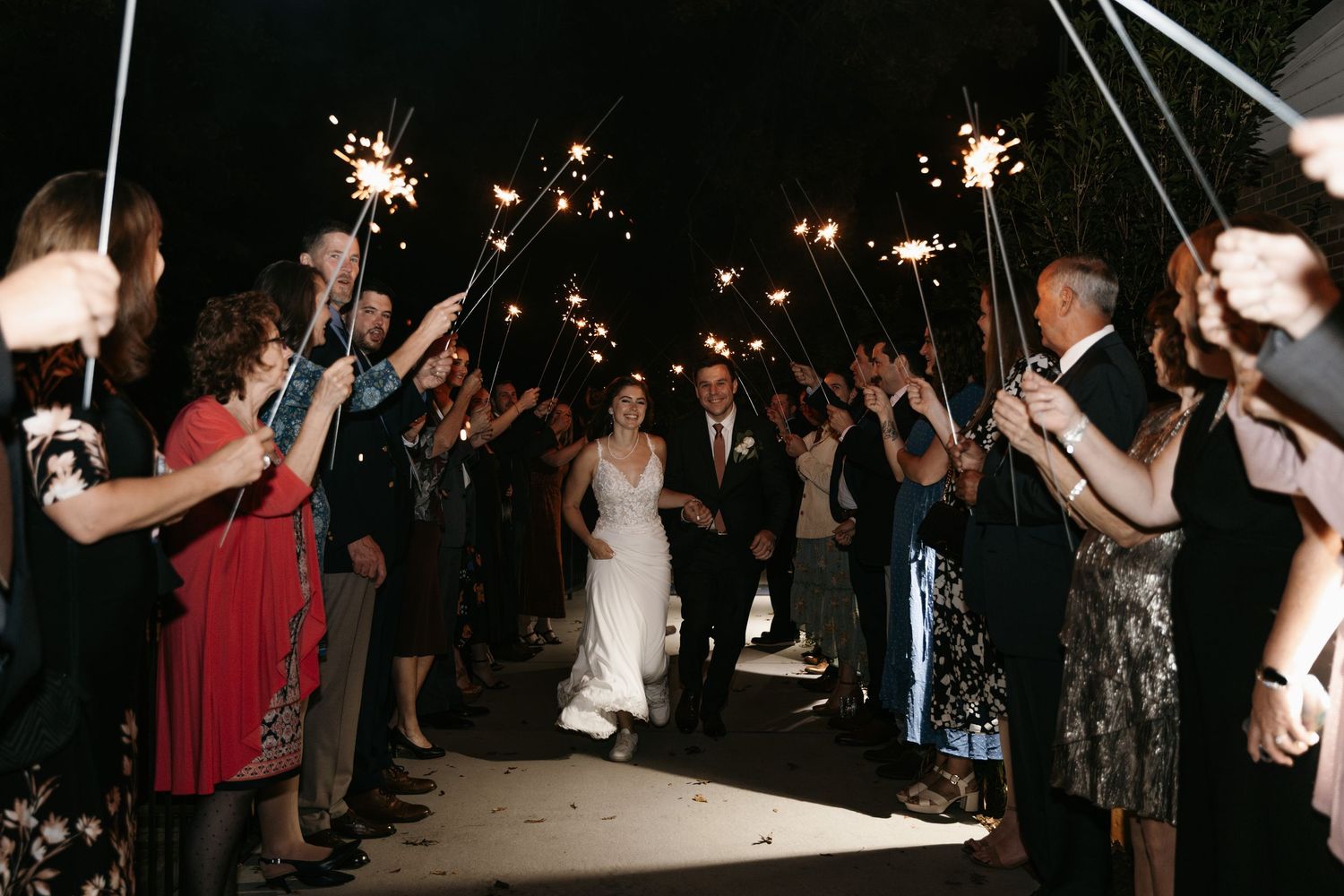Wedding guests form a sparkler tunnel exit for the newlyweds at night.
