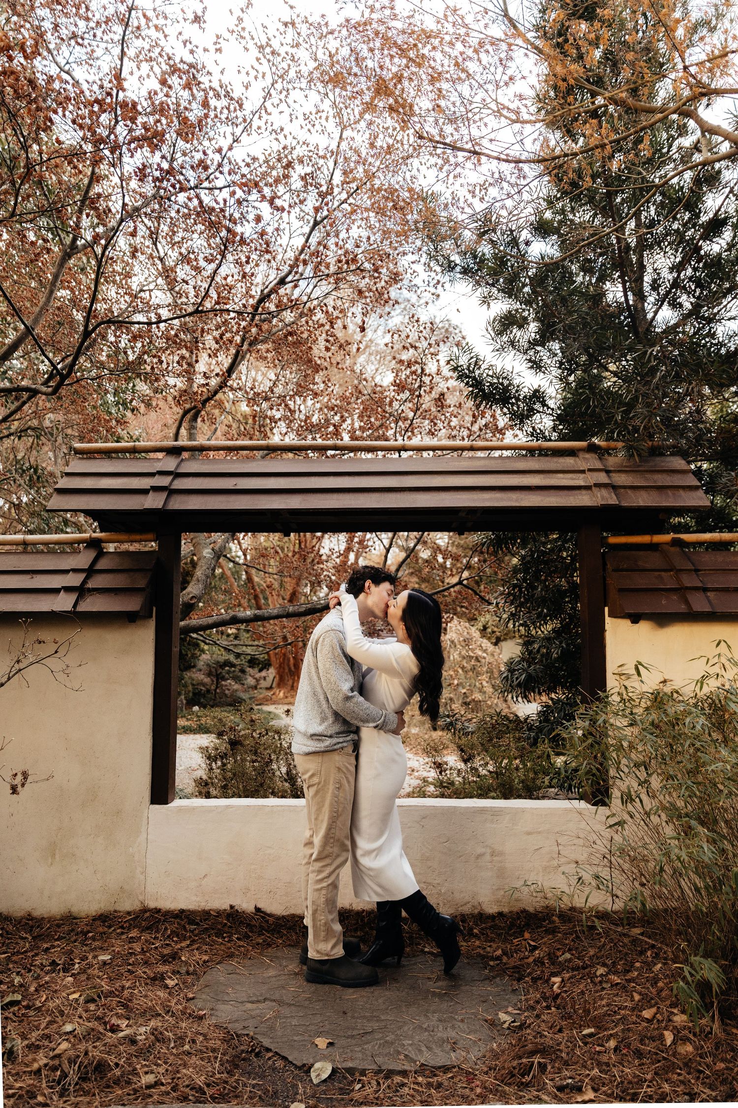 A couple shares a tender moment against a wall backdrop in an autumn setting.