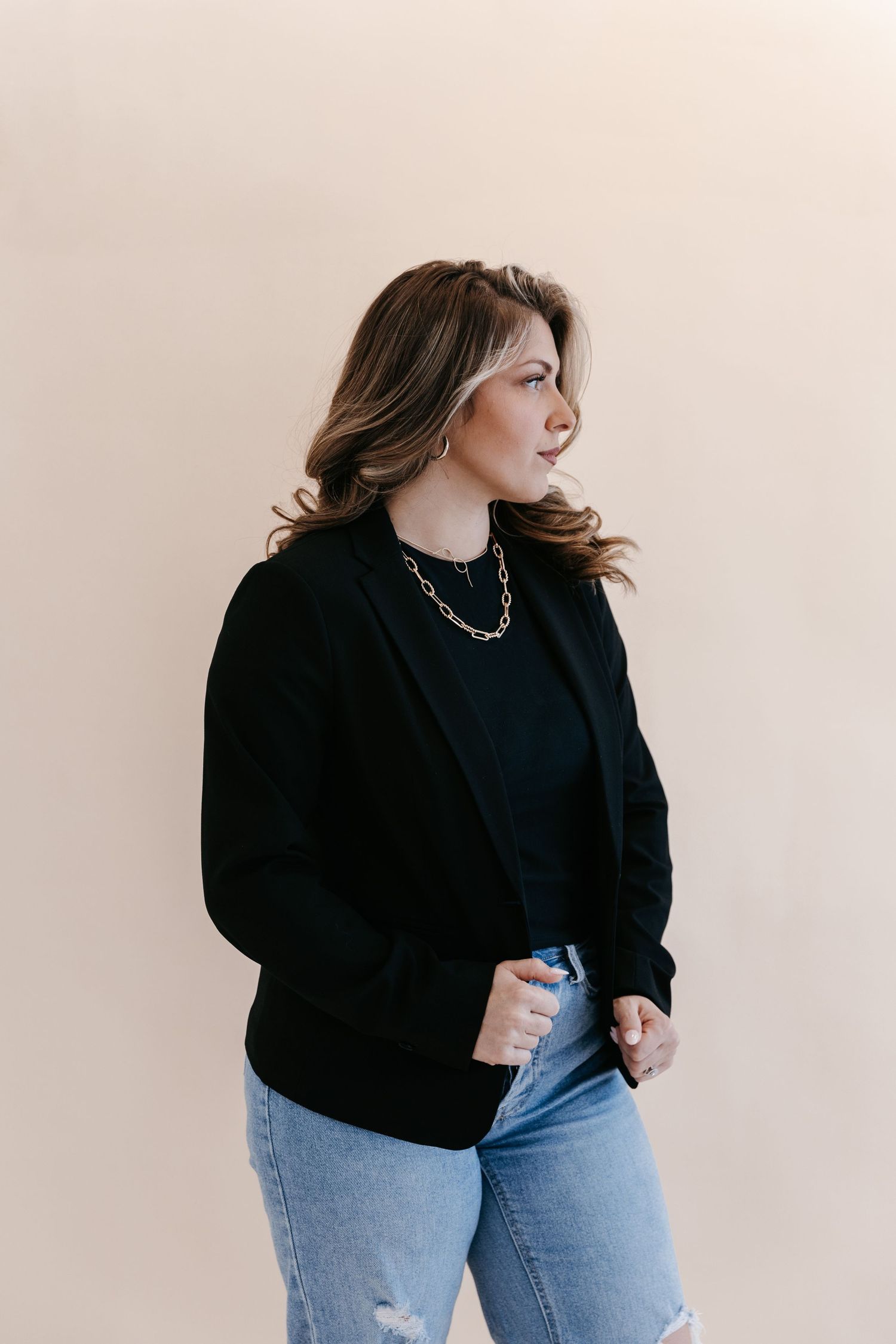 Professional portrait of a woman wearing a black blazer against beige background.