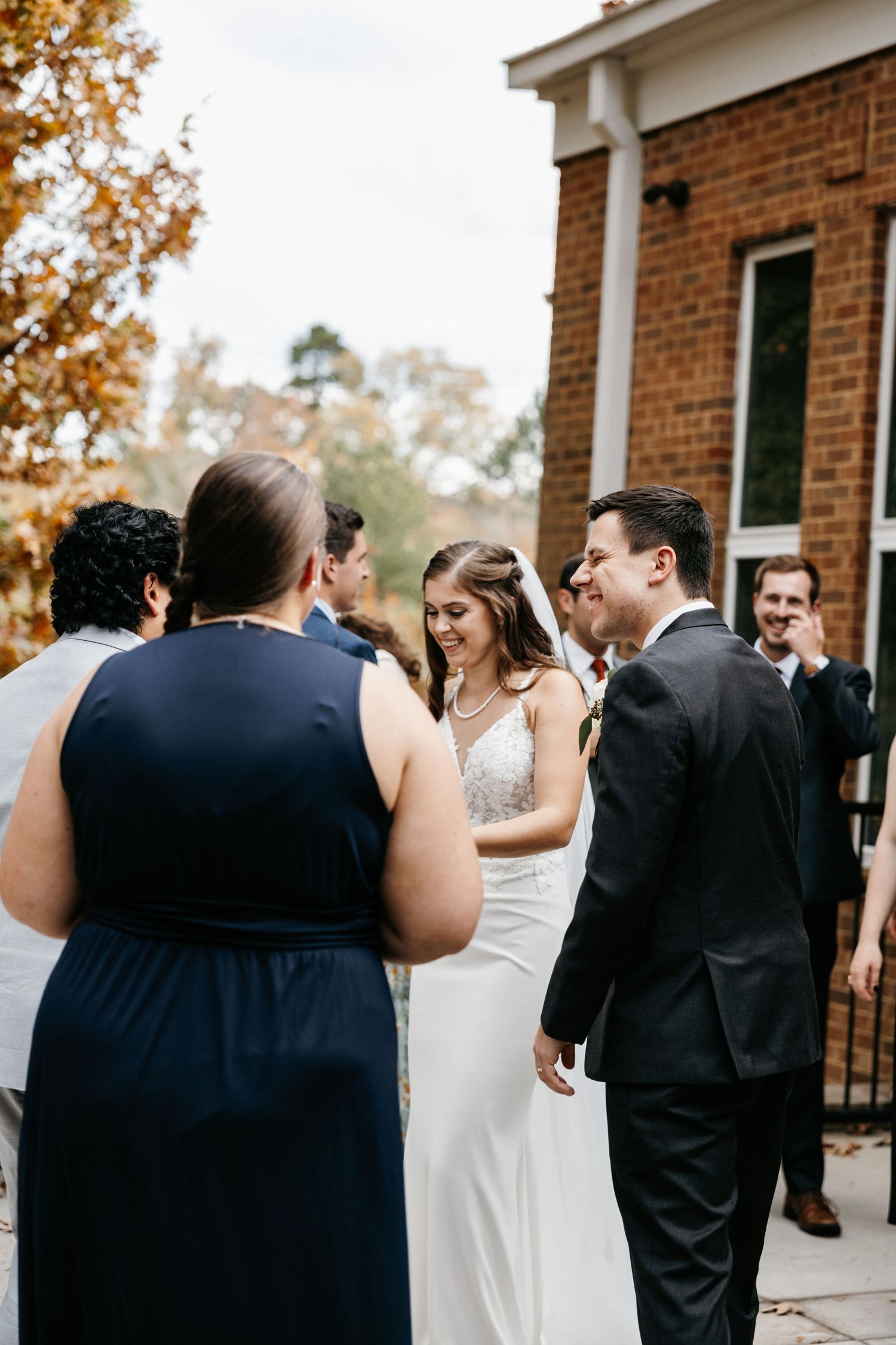 Wedding guests celebrating with bride and groom outside a brick church during autumn.