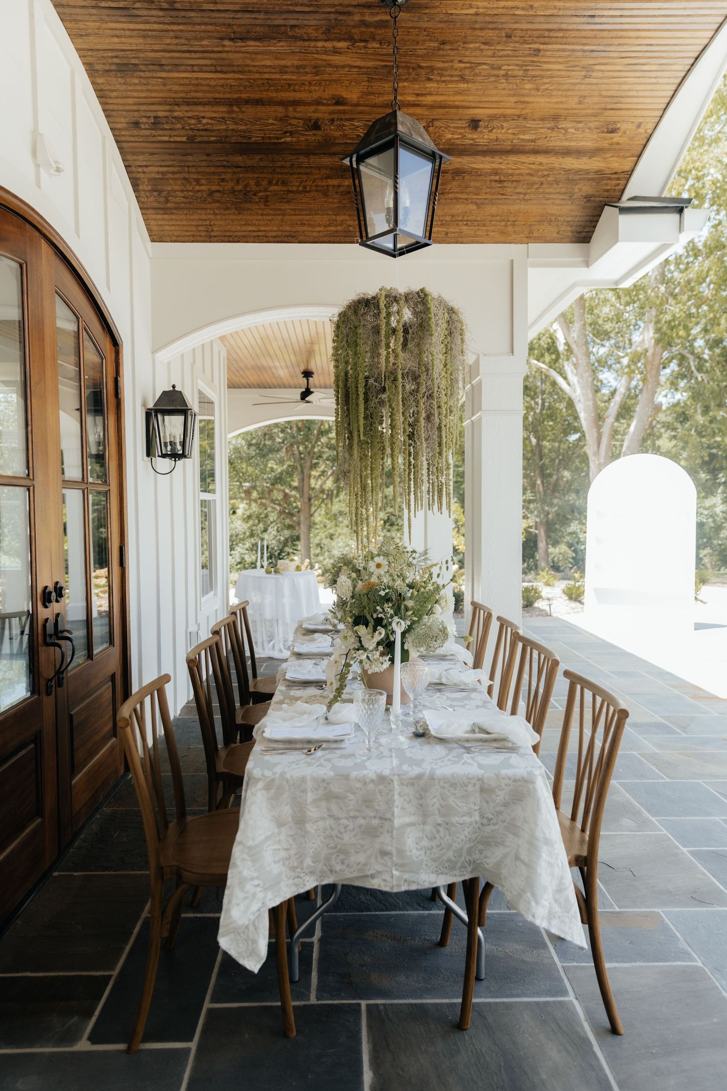 Covered dining area with wooden chairs and white tablecloths with hanging floral chandeliers.