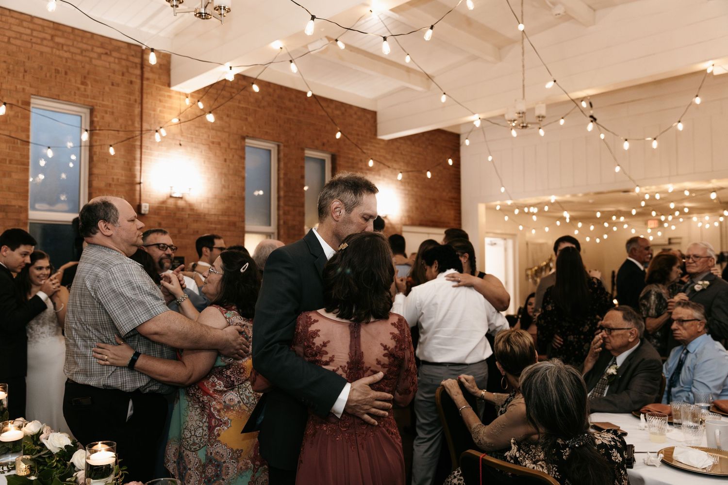 Wedding celebration with guests dancing under string lights in a rustic brick venue.