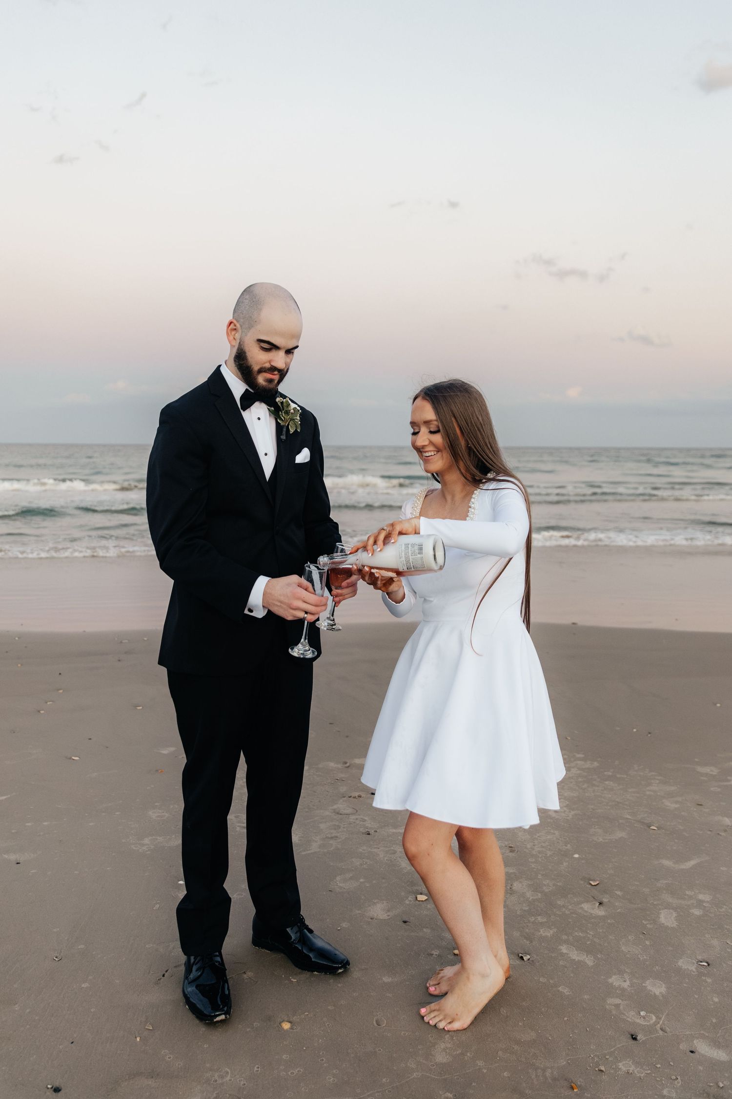 A couple pouring champagne together on the beach during their wedding celebration.