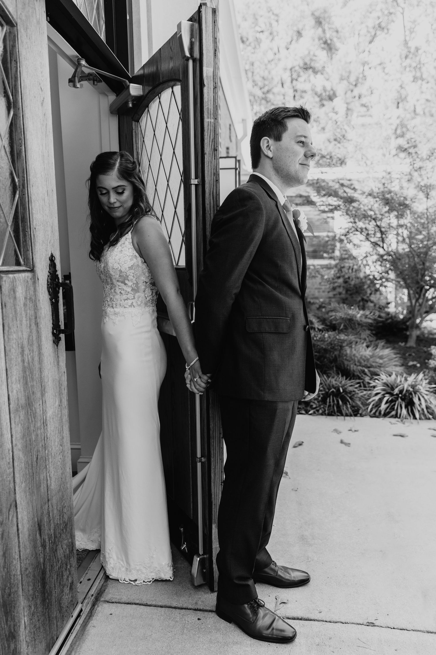 Wedding couple's emotional first look through wooden doorway at brick venue.