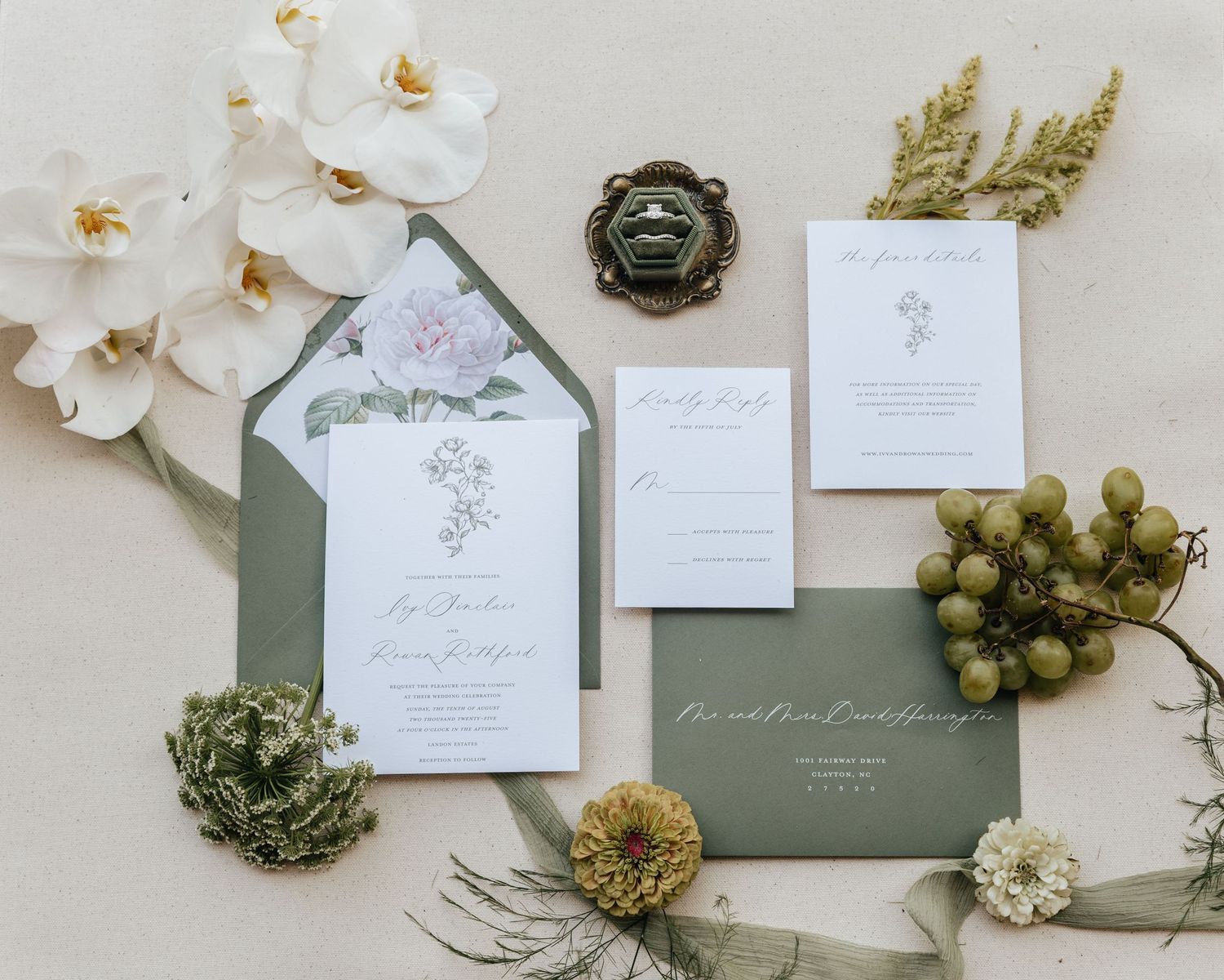 Wedding stationery set featuring sage green envelopes and white floral accents.