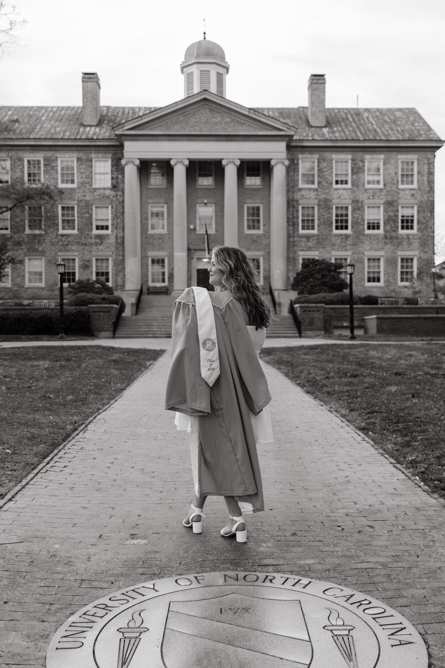 Graduate in cap and gown stands before University of North Carolina Chapel Hill building.
