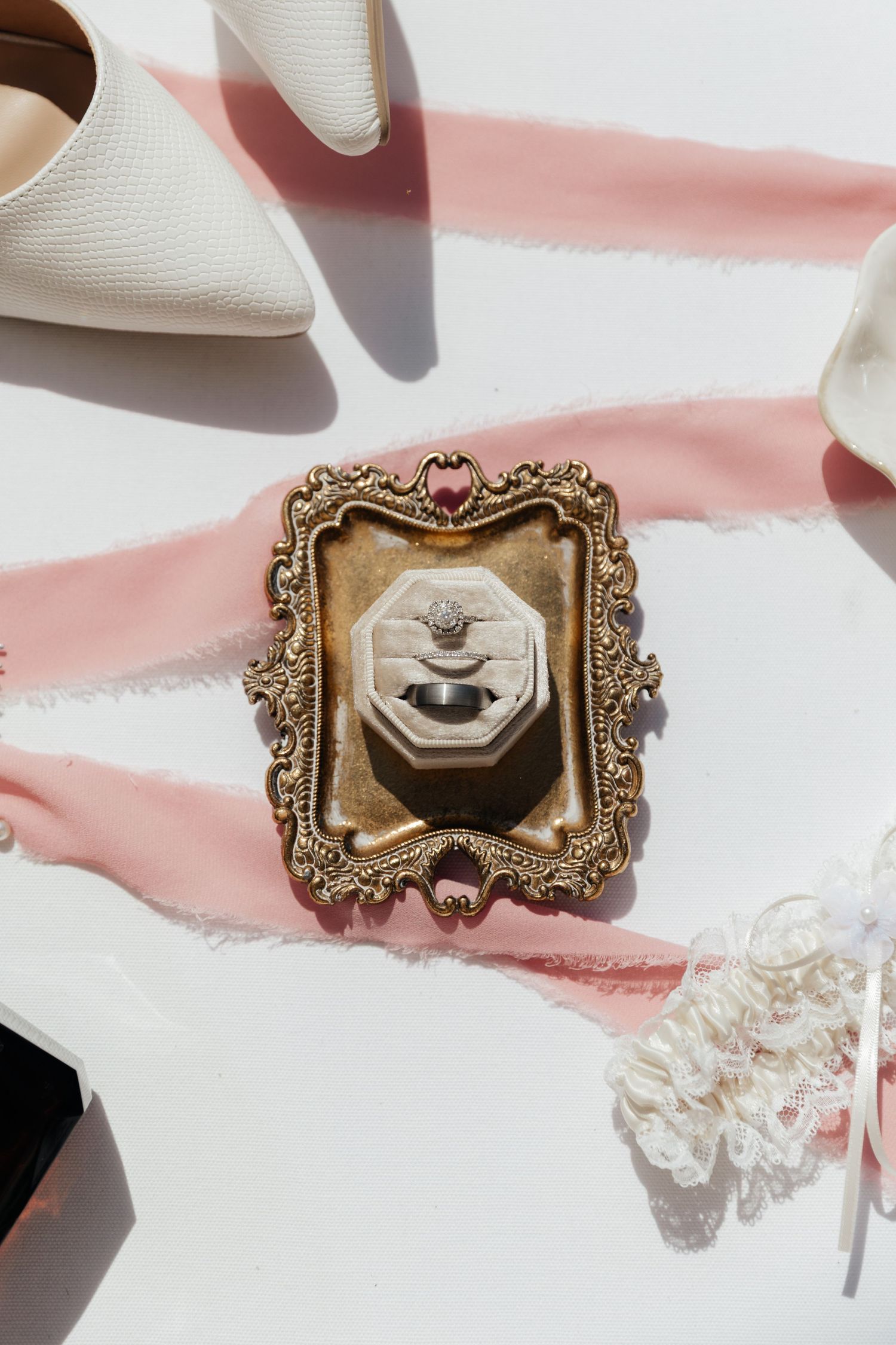 Vintage ornate frame with ring box styled with pink ribbon and bridal accessories.