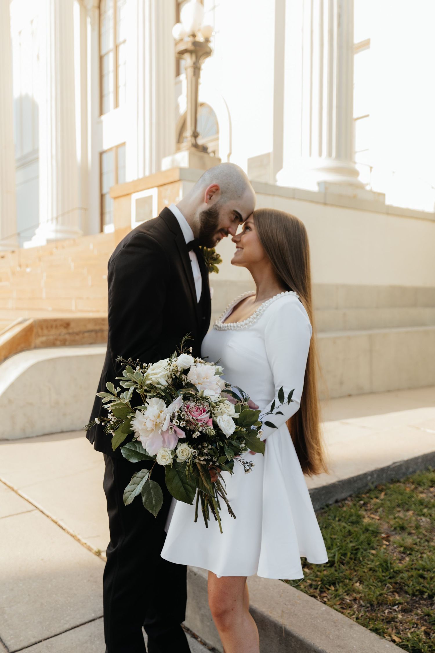 A romantic moment captured between a couple with white flowers against a classical building backdrop.