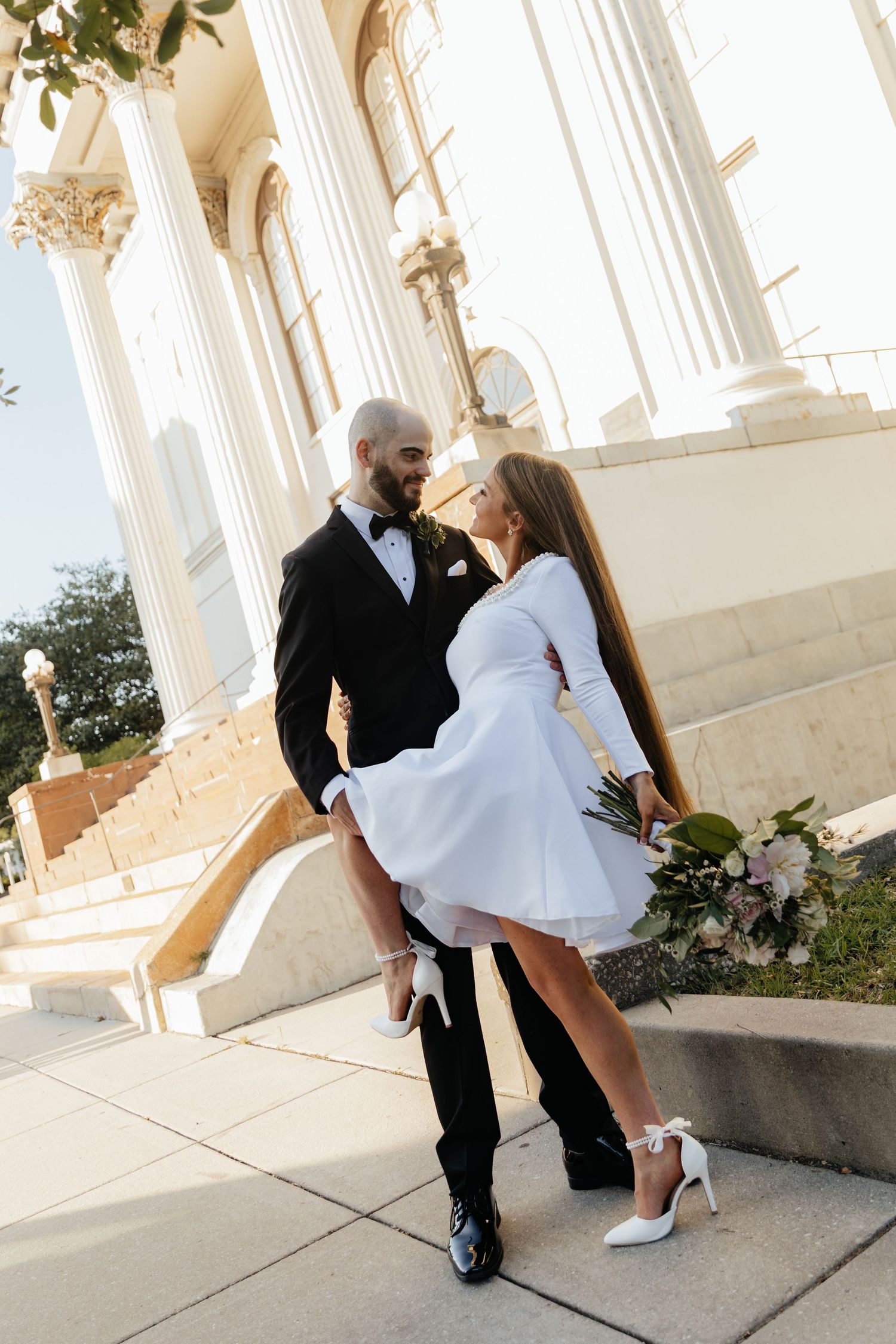 Elegant couple poses for romantic photos in front of a white columned building.