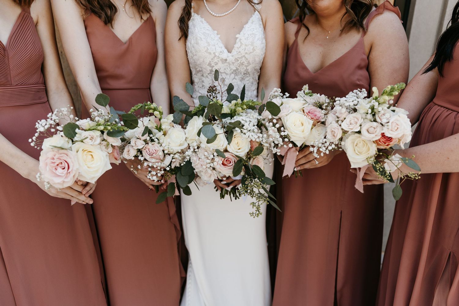 Row of bridesmaids in dusty rose dresses holding matching floral bouquets.