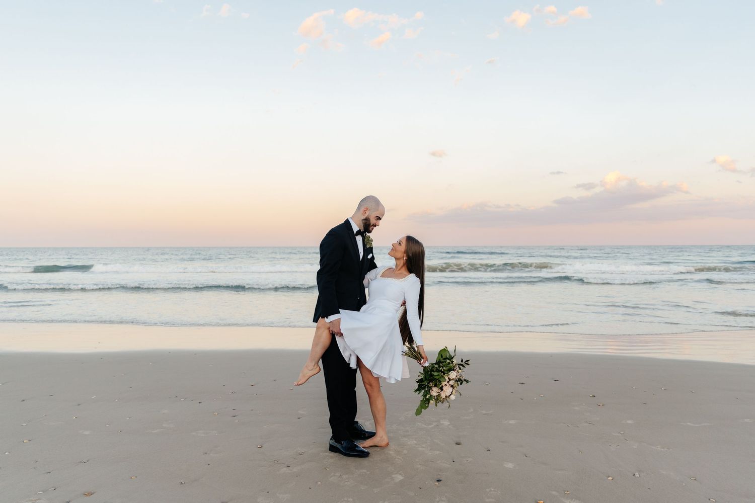Romantic sunset beach wedding portrait with waves crashing in background.
