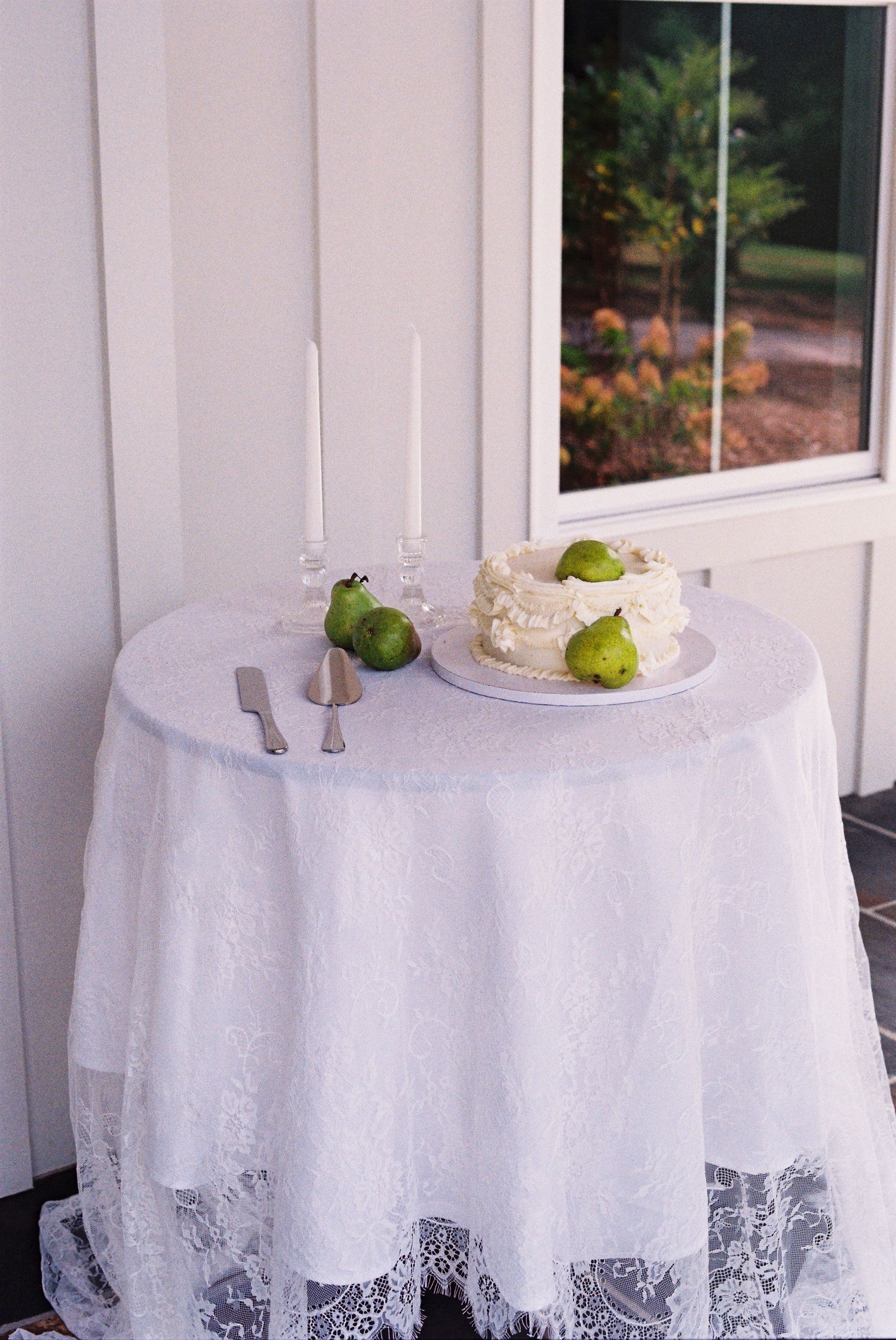 Elegant white lace tablecloths with green pears and floral decorations set for a wedding reception.