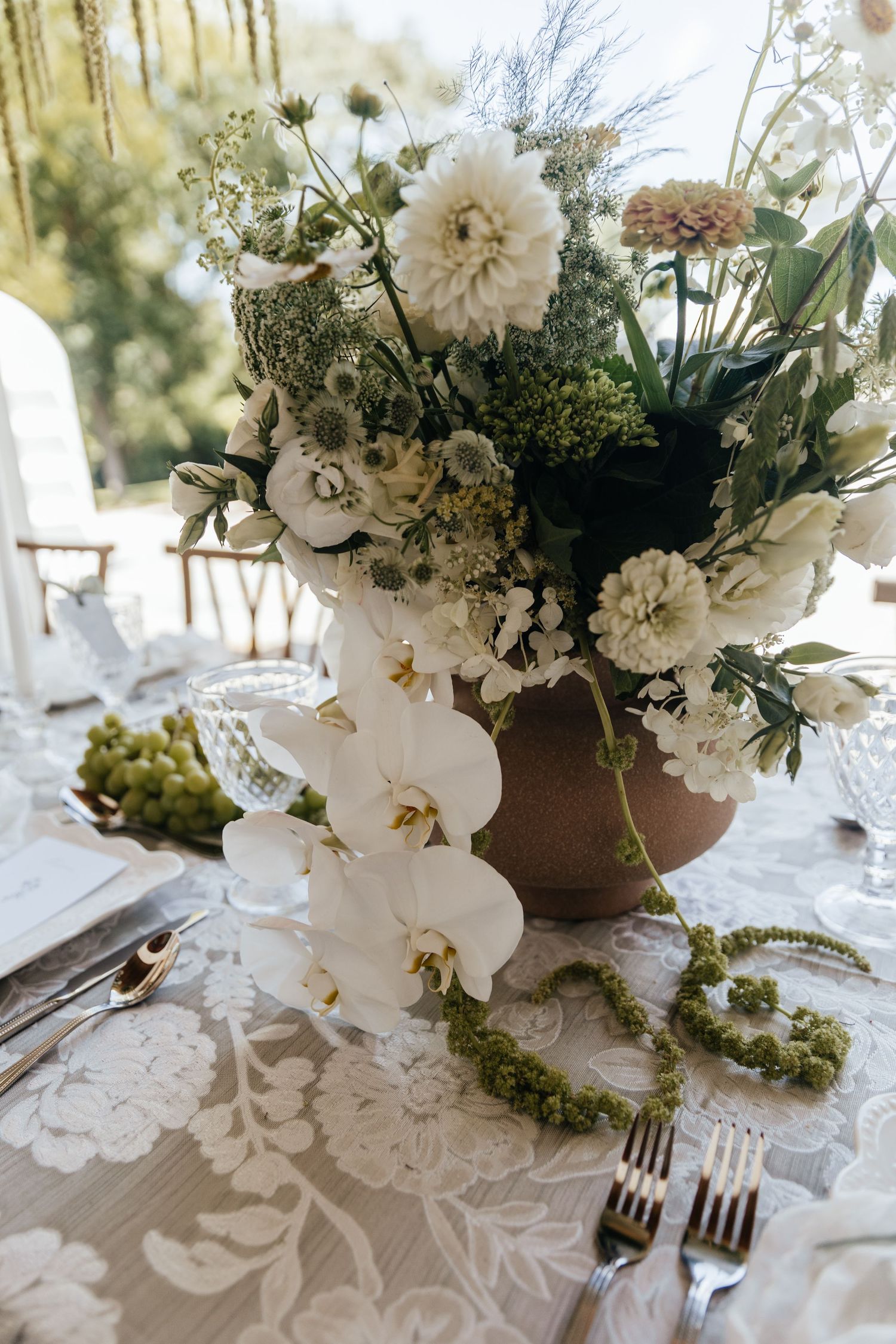 Elegant white floral centerpieces with orchids and dahlias arranged on a lace tablecloth.