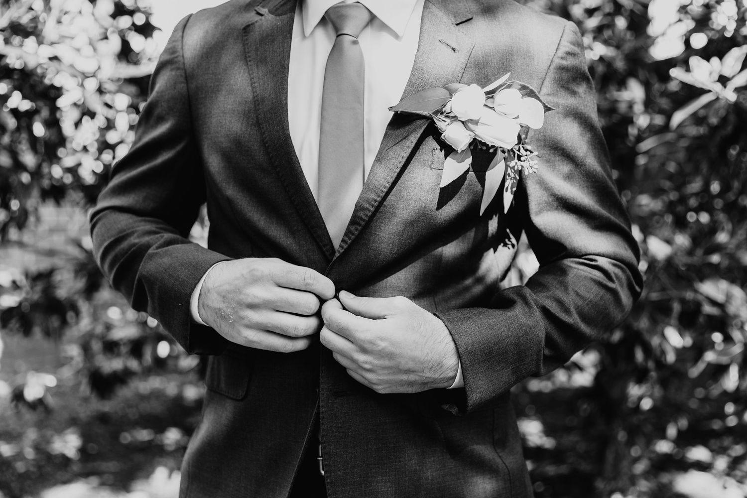 Groom in black suit adjusting his tie outdoors.