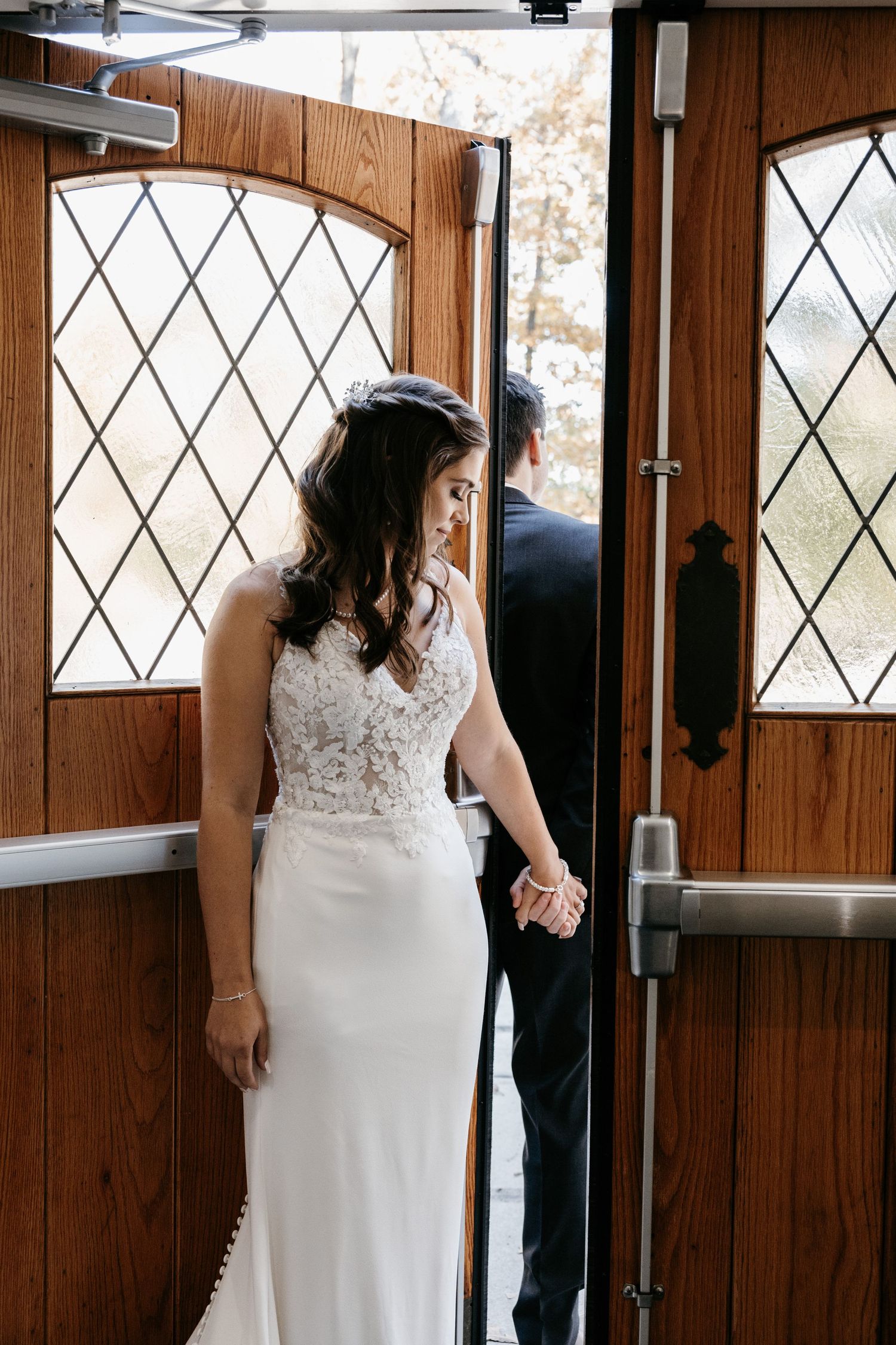Couple having their first look moment through a wooden door with diamond-patterned windows at a rustic venue.