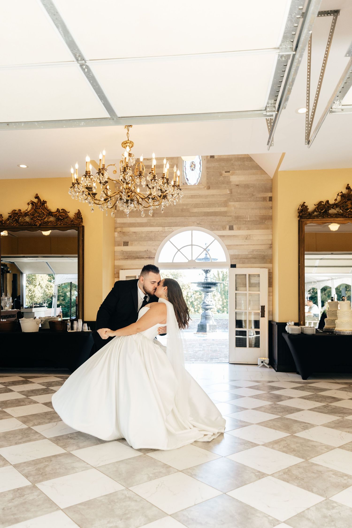 Couple dancing in spacious ballroom with elegant chandeliers and marble flooring.