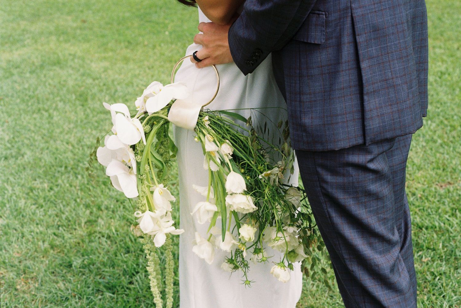 Newlyweds embrace during outdoor wedding photos with white bouquet and blue suit details.