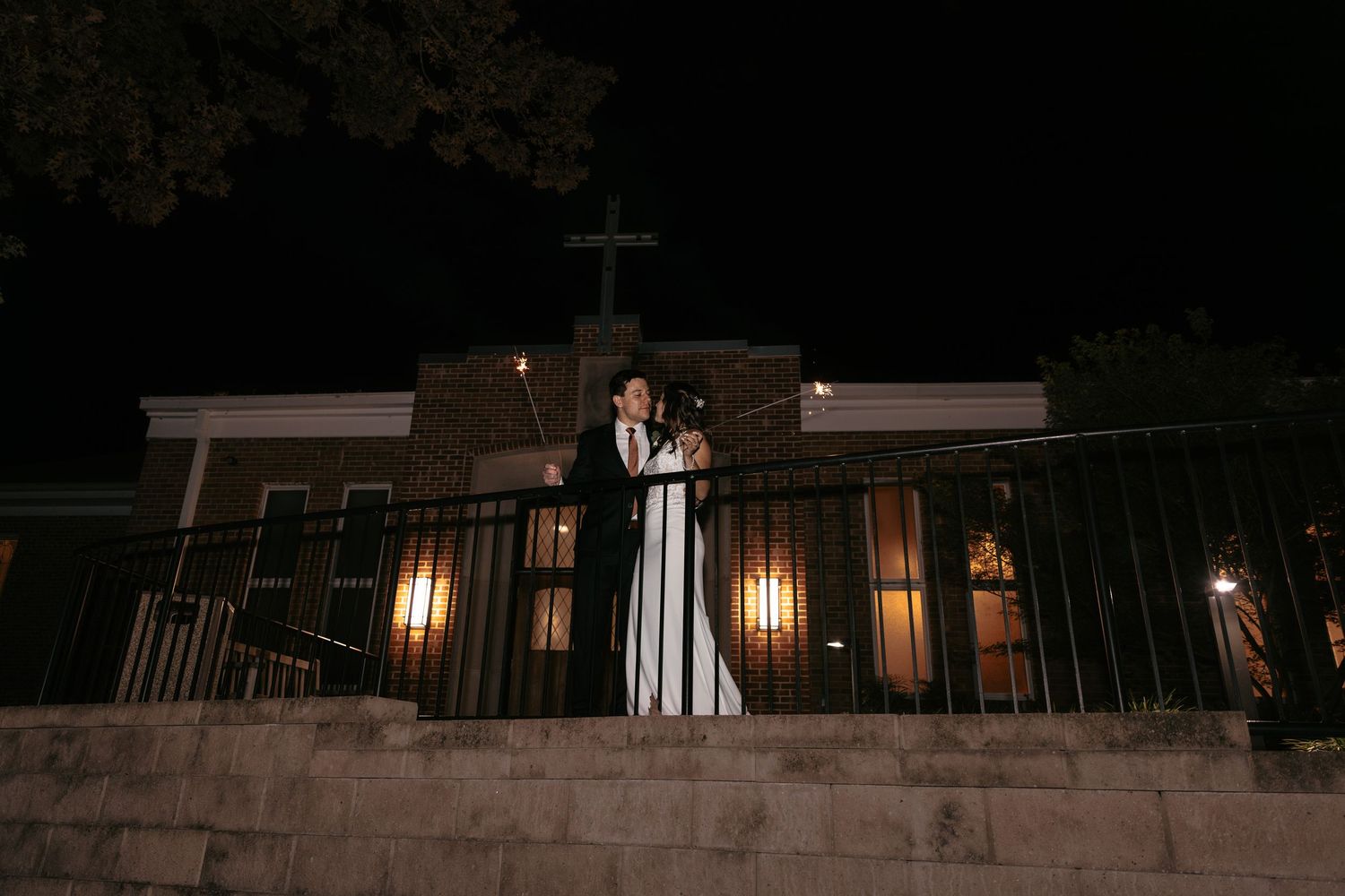 Couple embracing on a balcony at night with warm building lights in the background.
