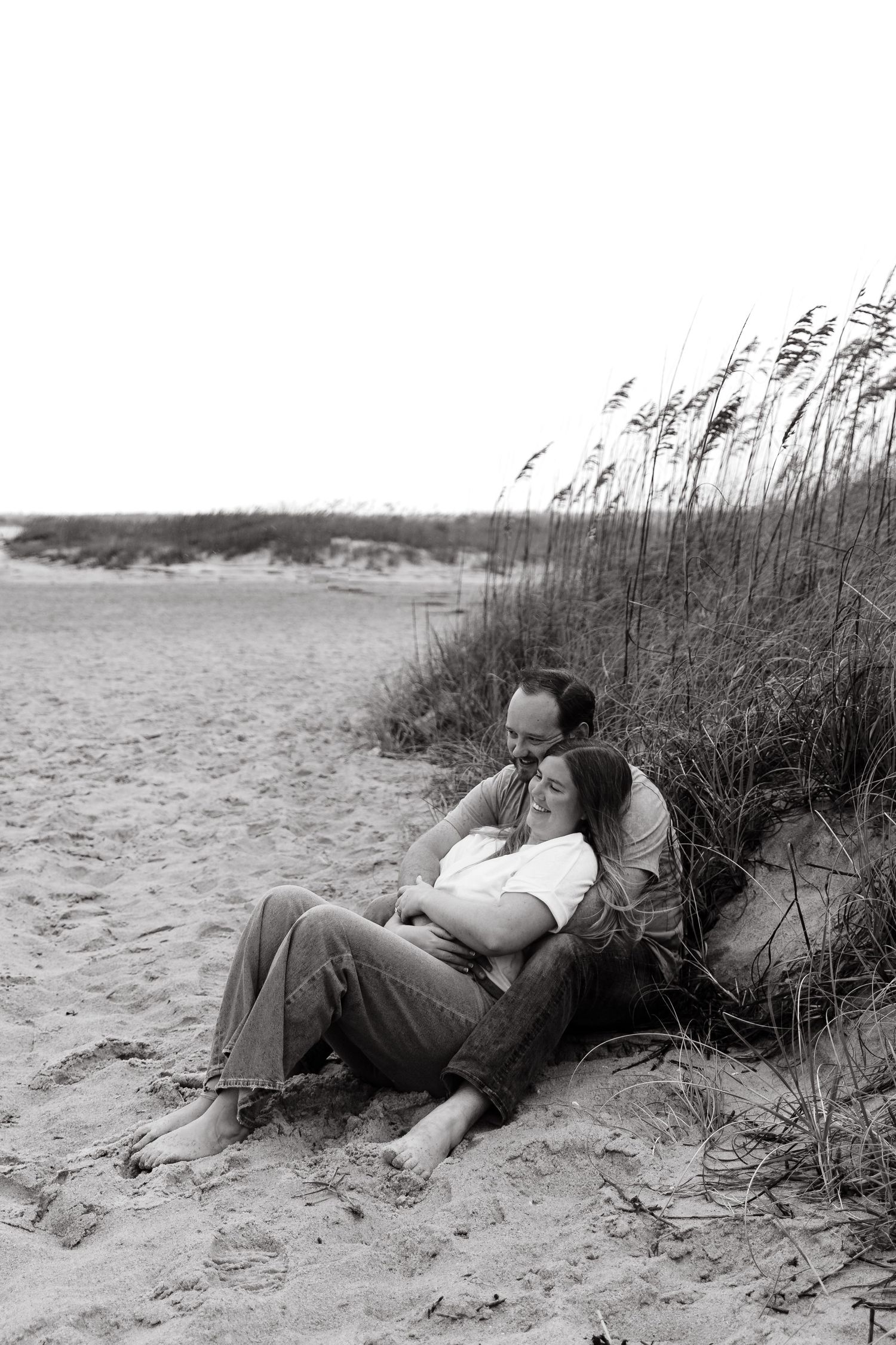 Couple relaxing together on sandy beach near tall grass.