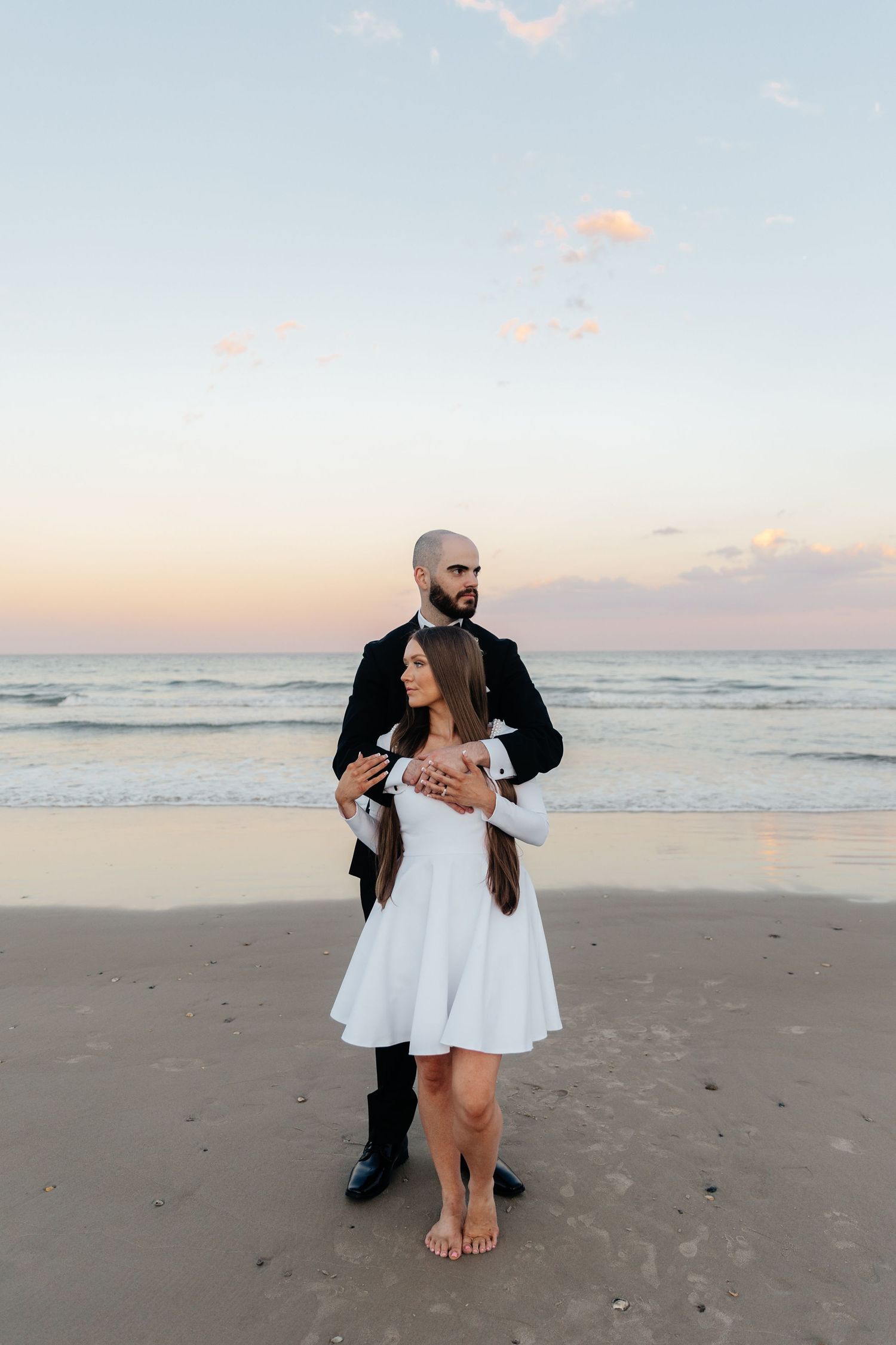 A romantic beach wedding scene with the couple dancing in formal attire at sunset.