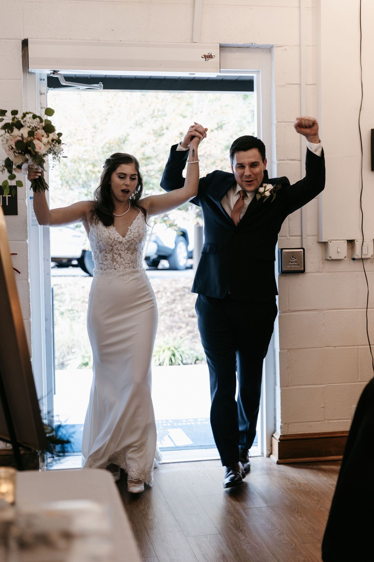 Wedding couple makes grand entrance into reception venue with arms raised in celebration.